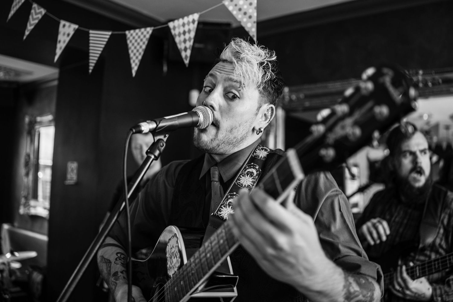 Black and white photo of musicians performing on stage with bunting decorations overhead.