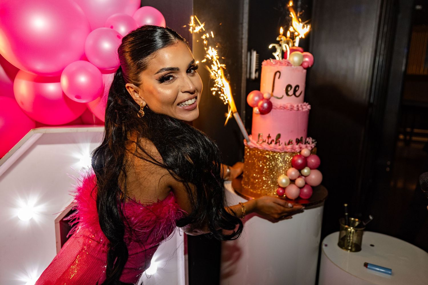 Birthday celebration with pink balloons and lit cake in dark room.