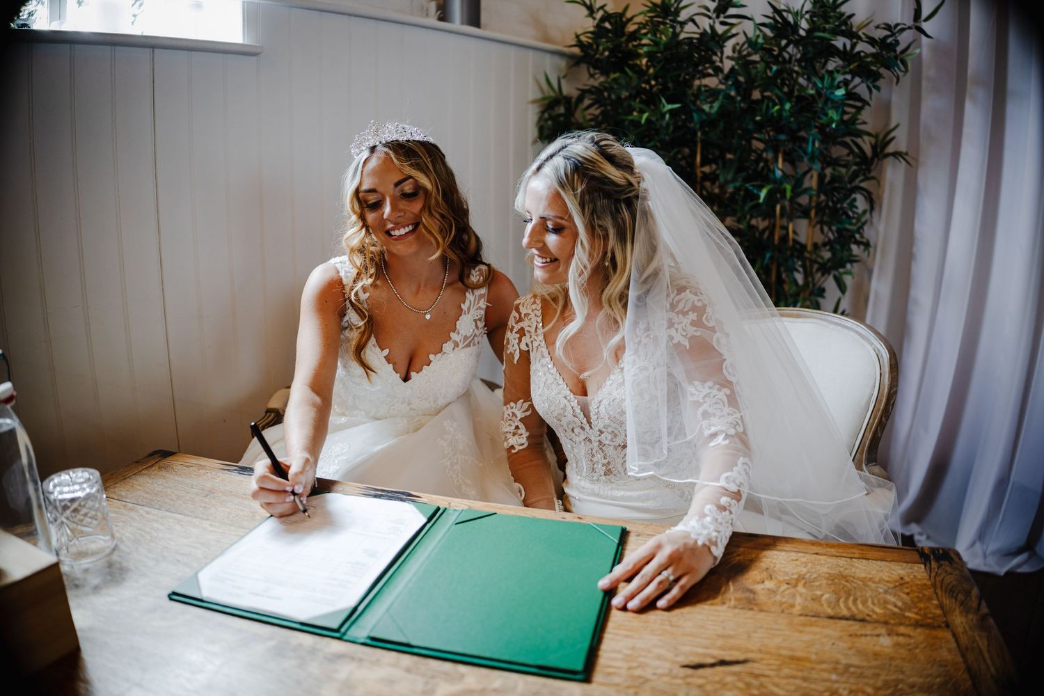 A bride signs official documents at a desk during a wedding ceremony in a bright interior space.