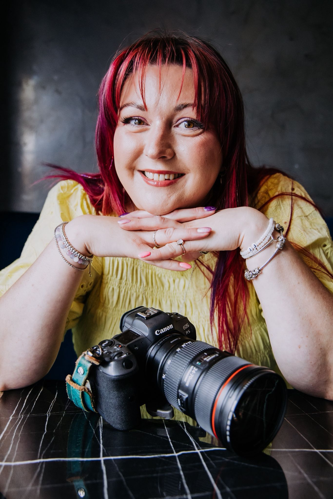 A series of photos showing someone with red hair in a yellow top posing playfully with a professional camera on a dark surface.