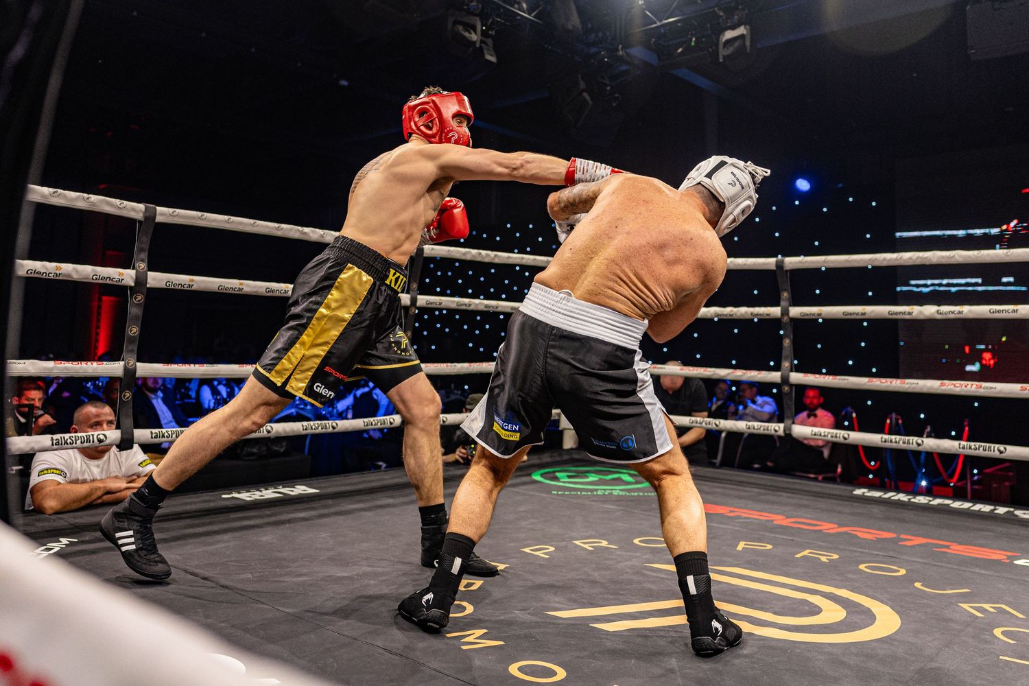 Two boxers wearing headgear exchange punches in a professional boxing ring during a competitive match.