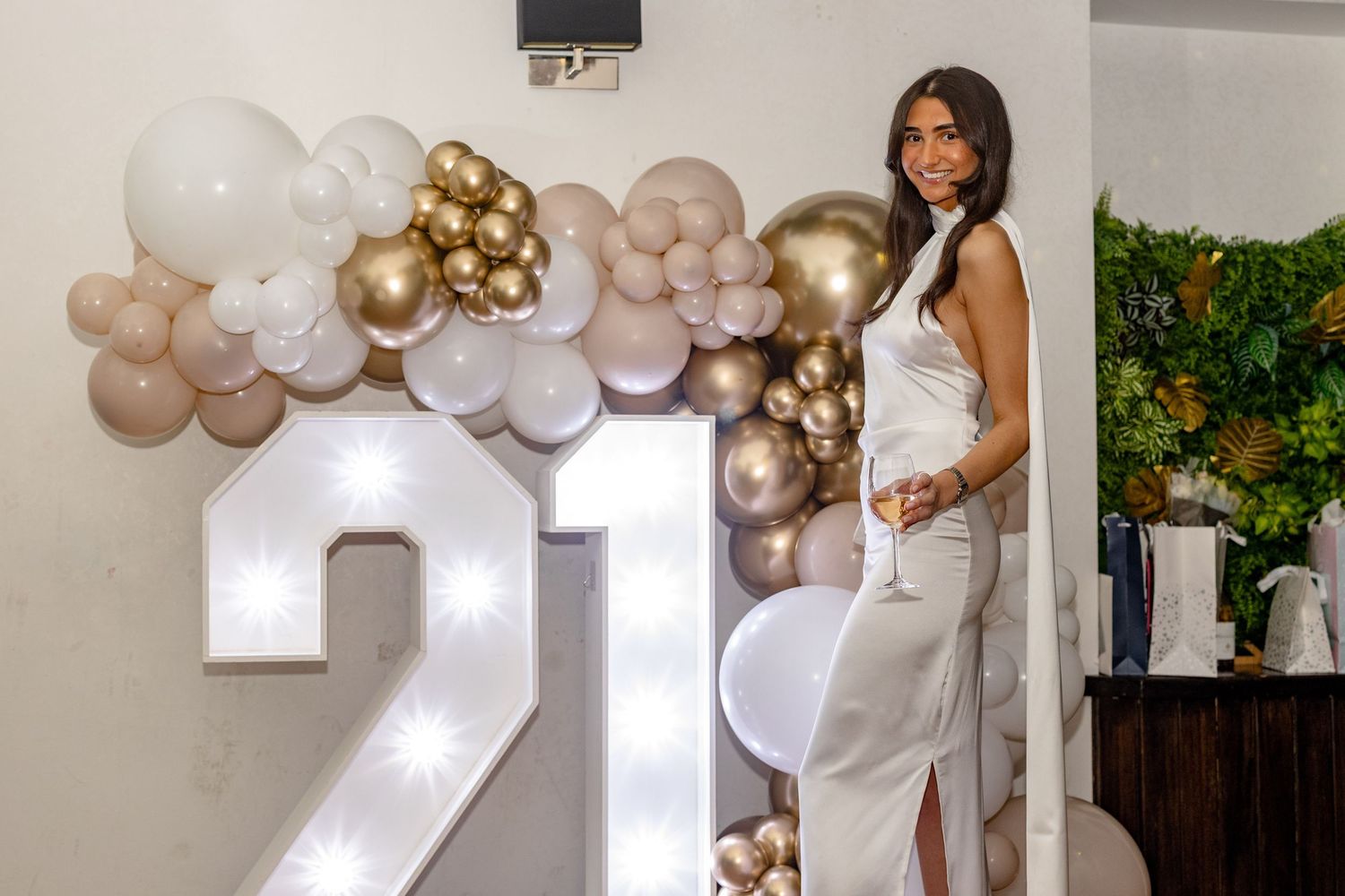 A 21st birthday celebration with gold and white balloon decorations and illuminated numbers.