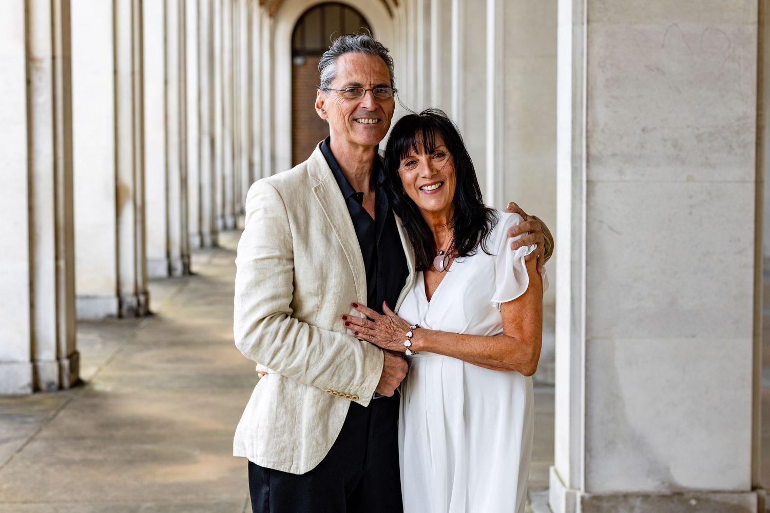 Wedding couple and guests celebrate in an elegant colonnade with white pillars and natural lighting.