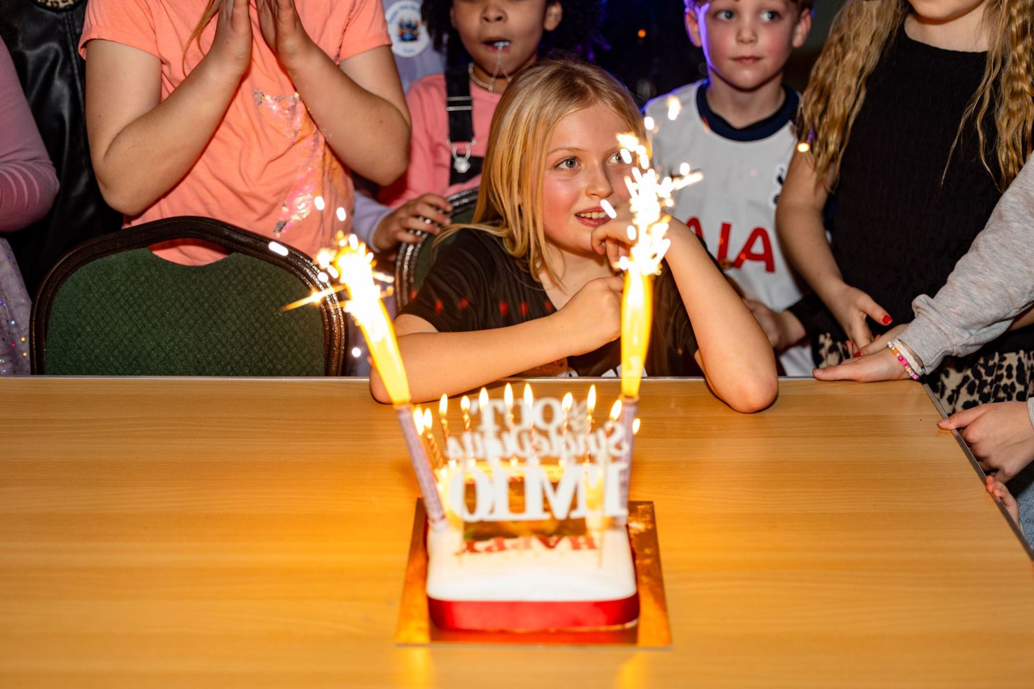 A birthday cake with sparklers glowing brightly on a wooden table during a celebration.