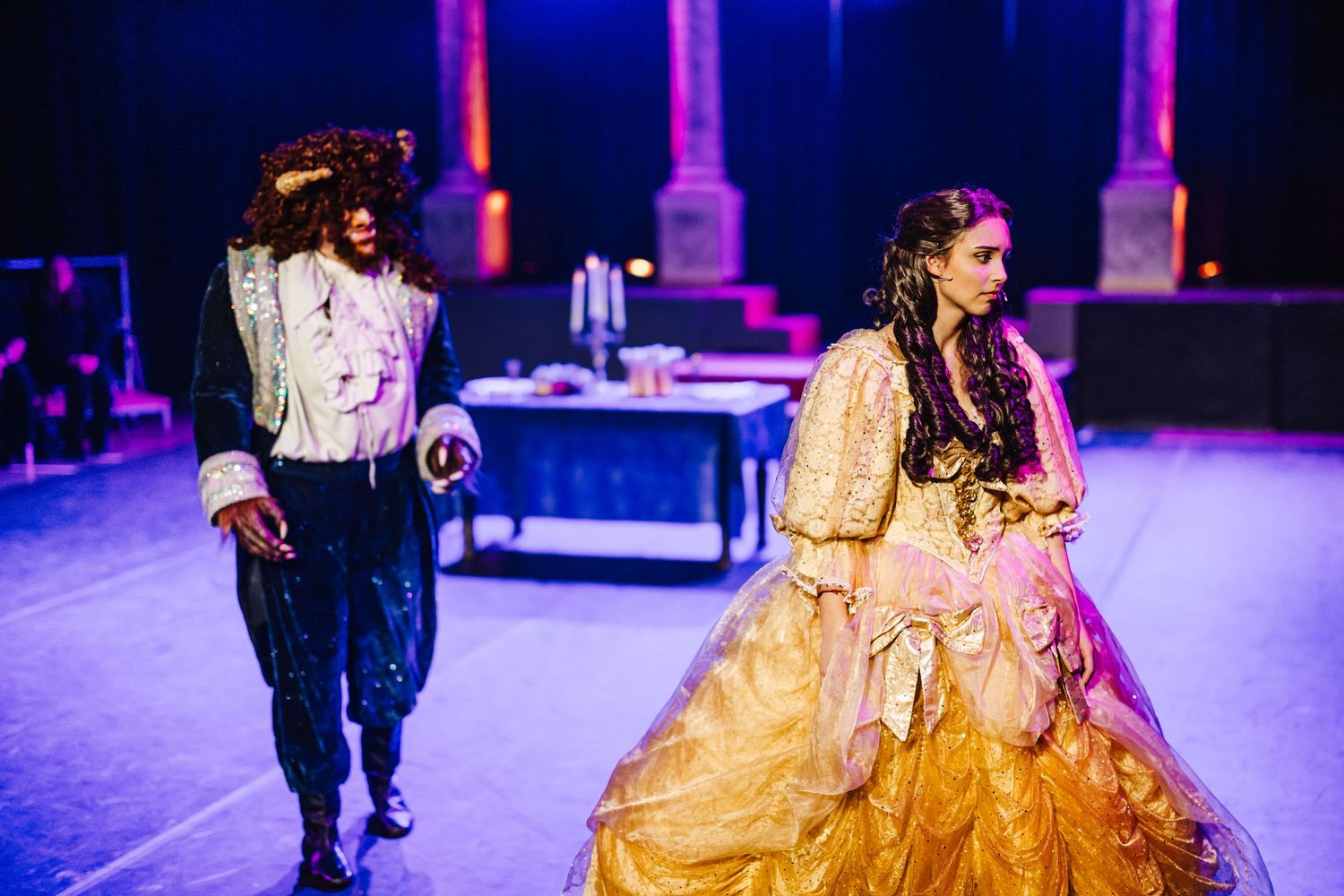 Dancers perform in elegant costumes under dramatic purple stage lighting at a theatrical production.