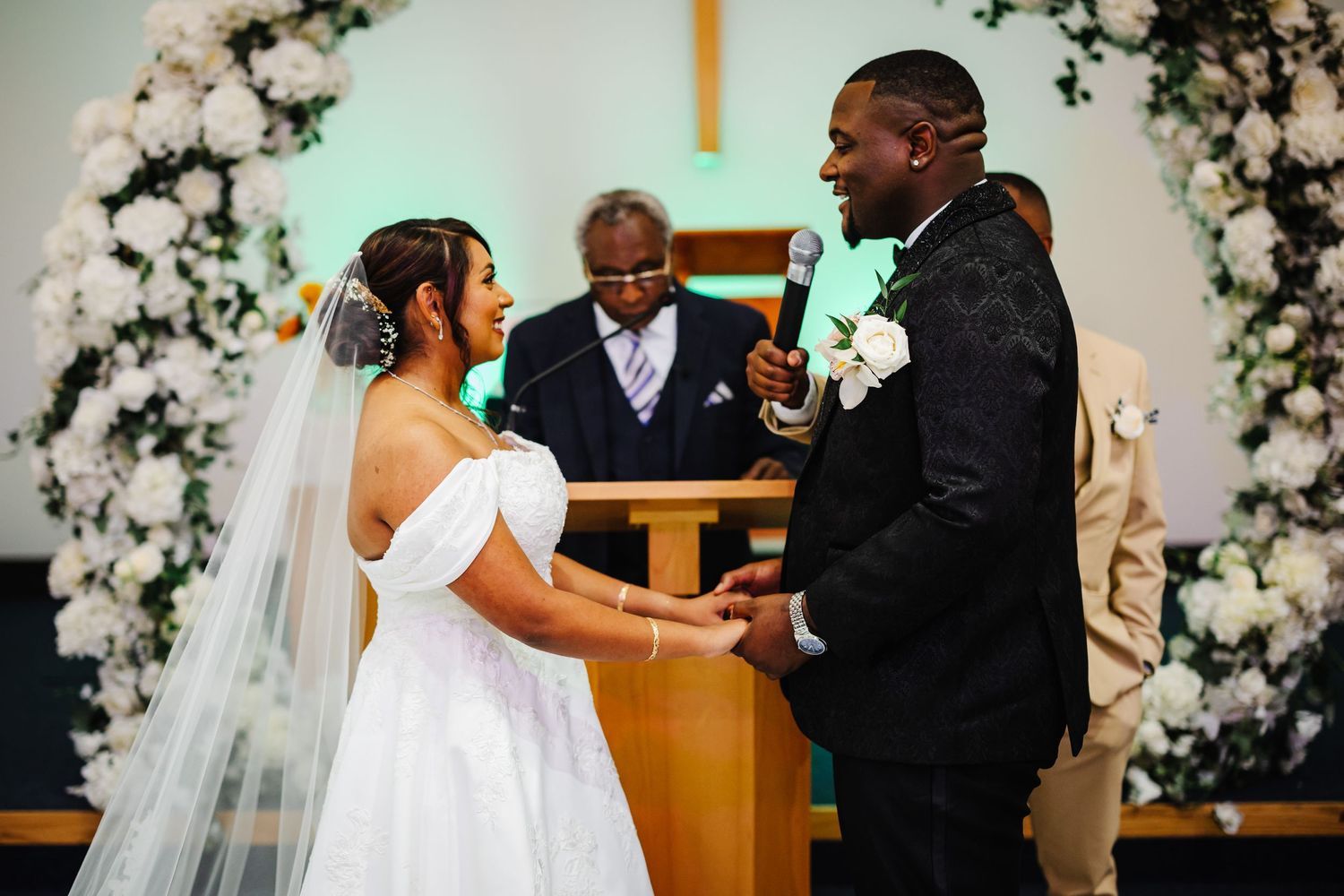 Wedding ceremony in church with white floral arch and romantic lighting.