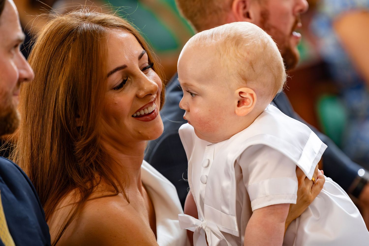 A joyful moment shared between a baby in white and someone during a special occasion.
