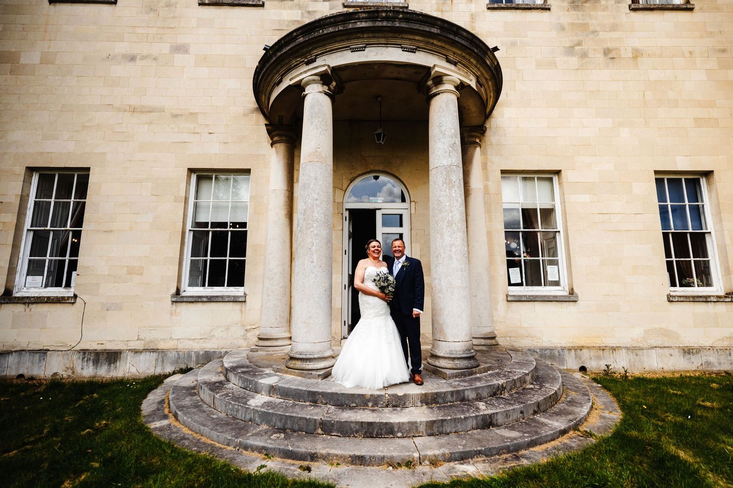 Elegant stone building with classical columns and symmetrical windows creates perfect wedding backdrop.