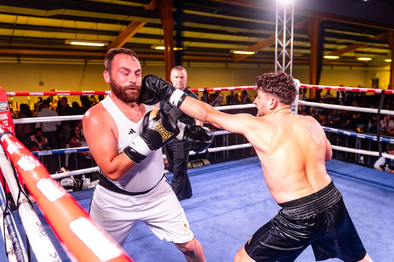 Two boxers exchange punches during an intense match in a boxing ring under bright arena lights.
