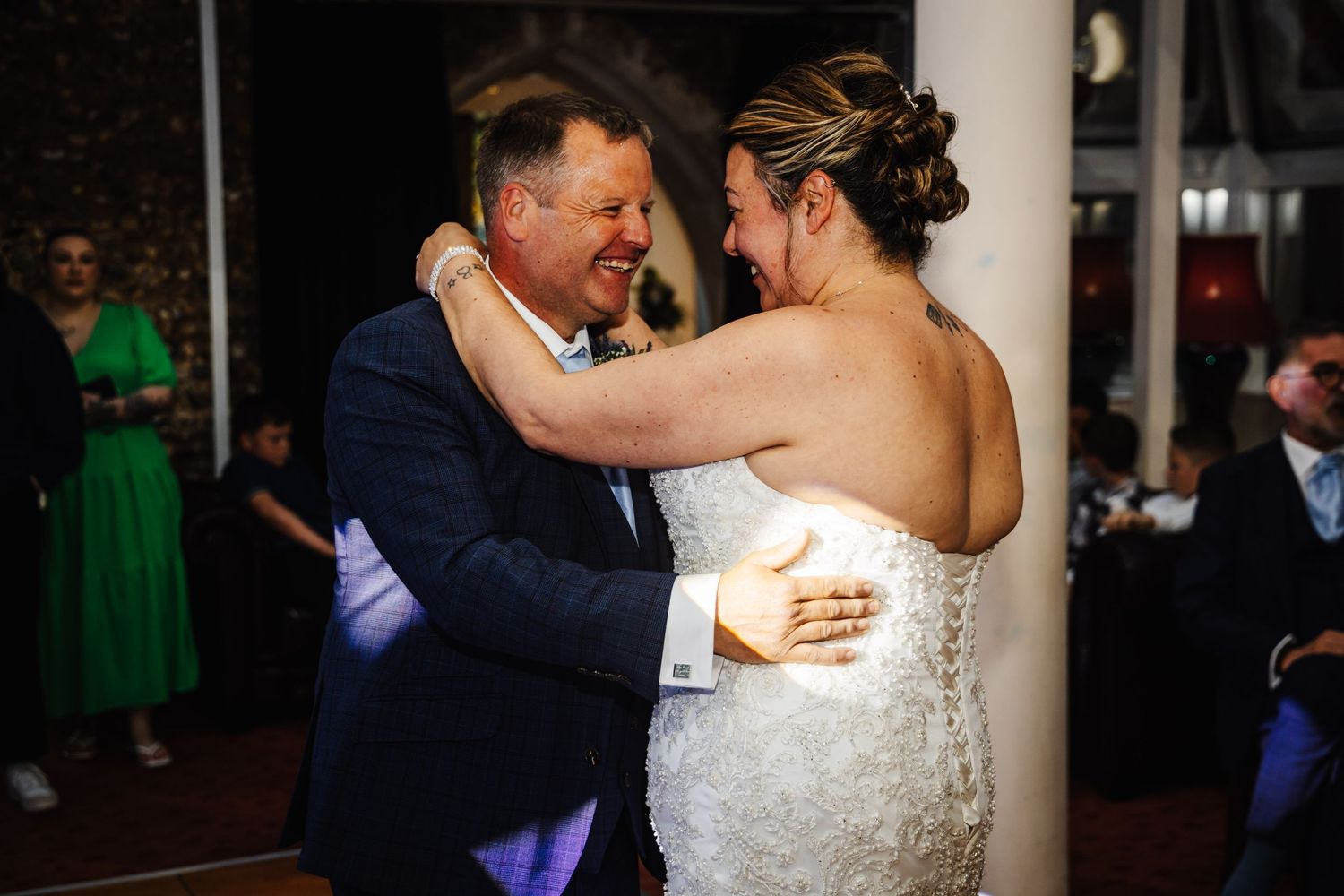 A couple shares a romantic dance moment at an evening wedding reception with guests watching in the background.