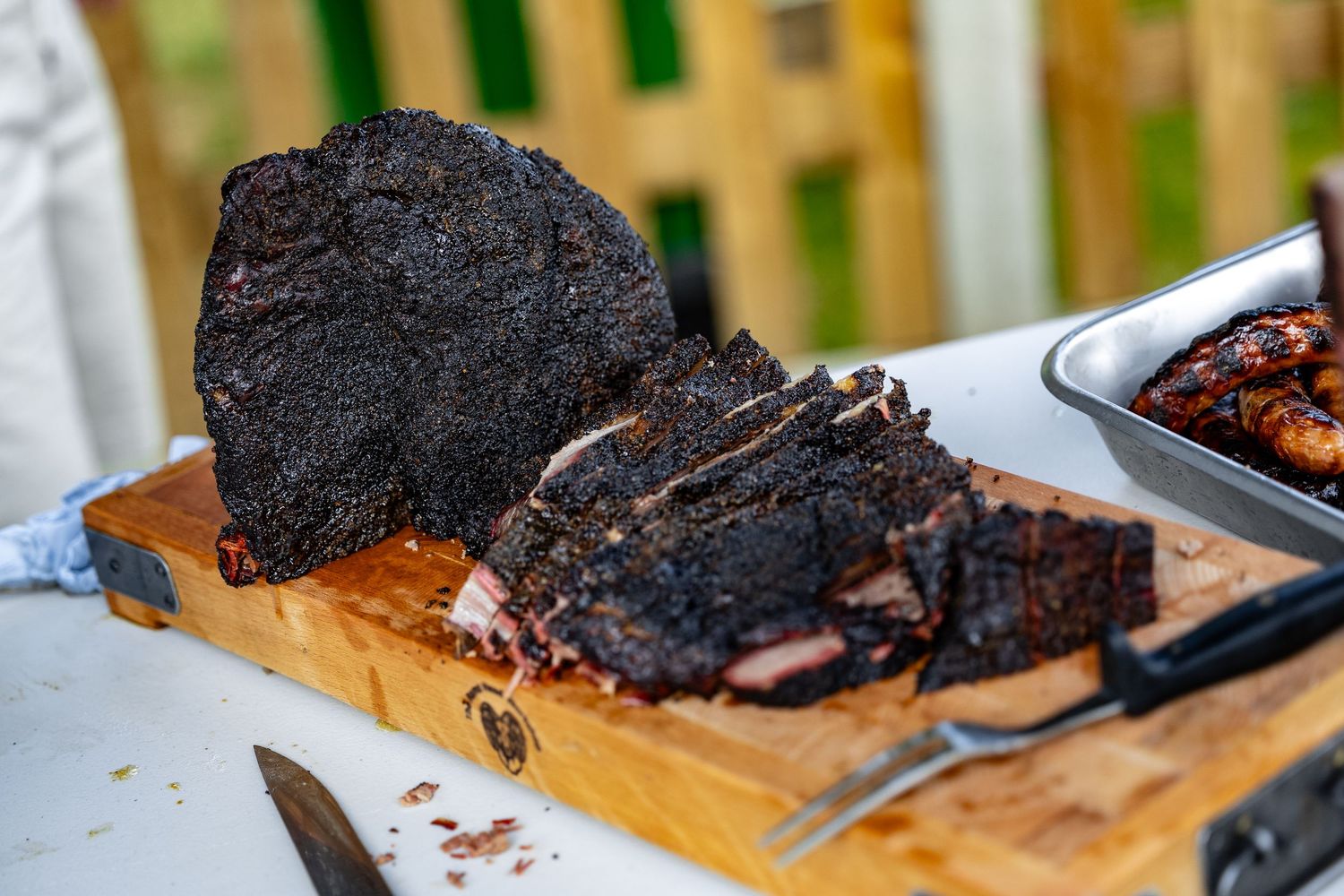 Slices of smoked brisket being cut on a wooden cutting board with a sharp knife.