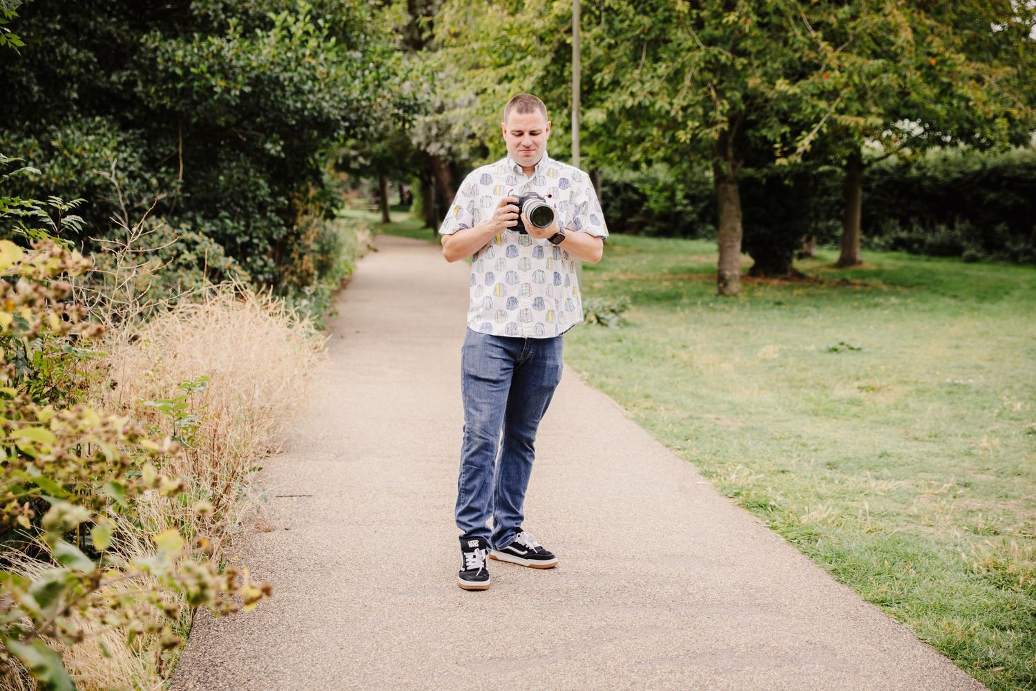 A person's feet and legs shown walking along a winding path through a green park on a sunny day.