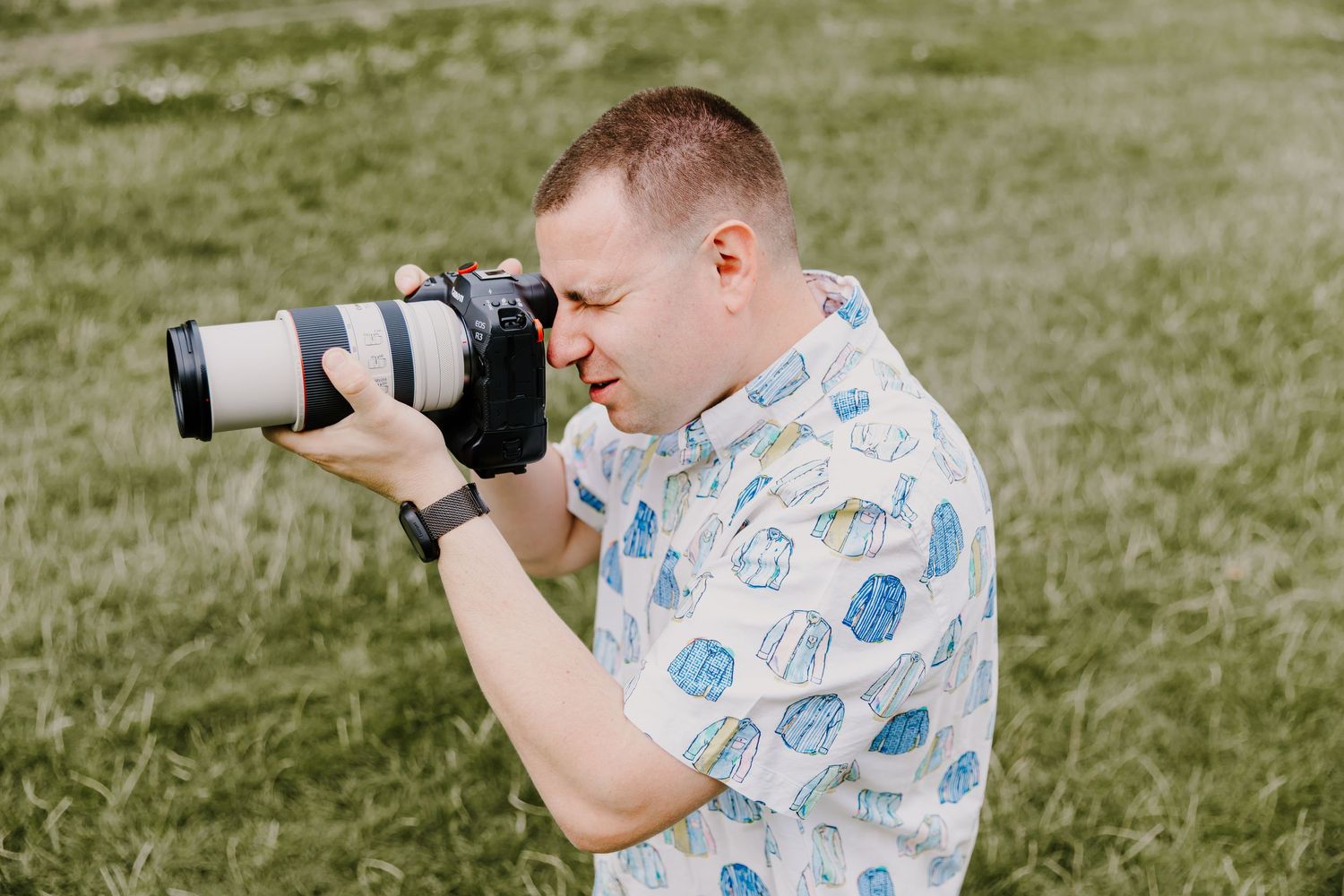 A photographer wearing a patterned shirt taking pictures with a telephoto lens outdoors.
