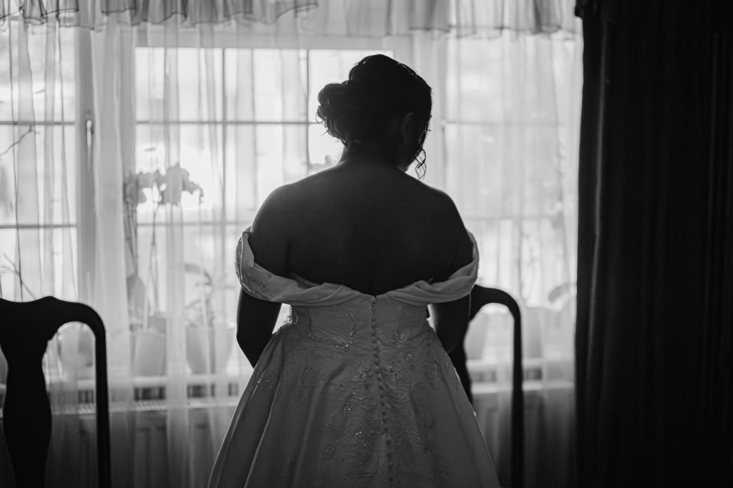 Silhouettes of figures against a bright window with sheer curtains creating a dramatic contrast.