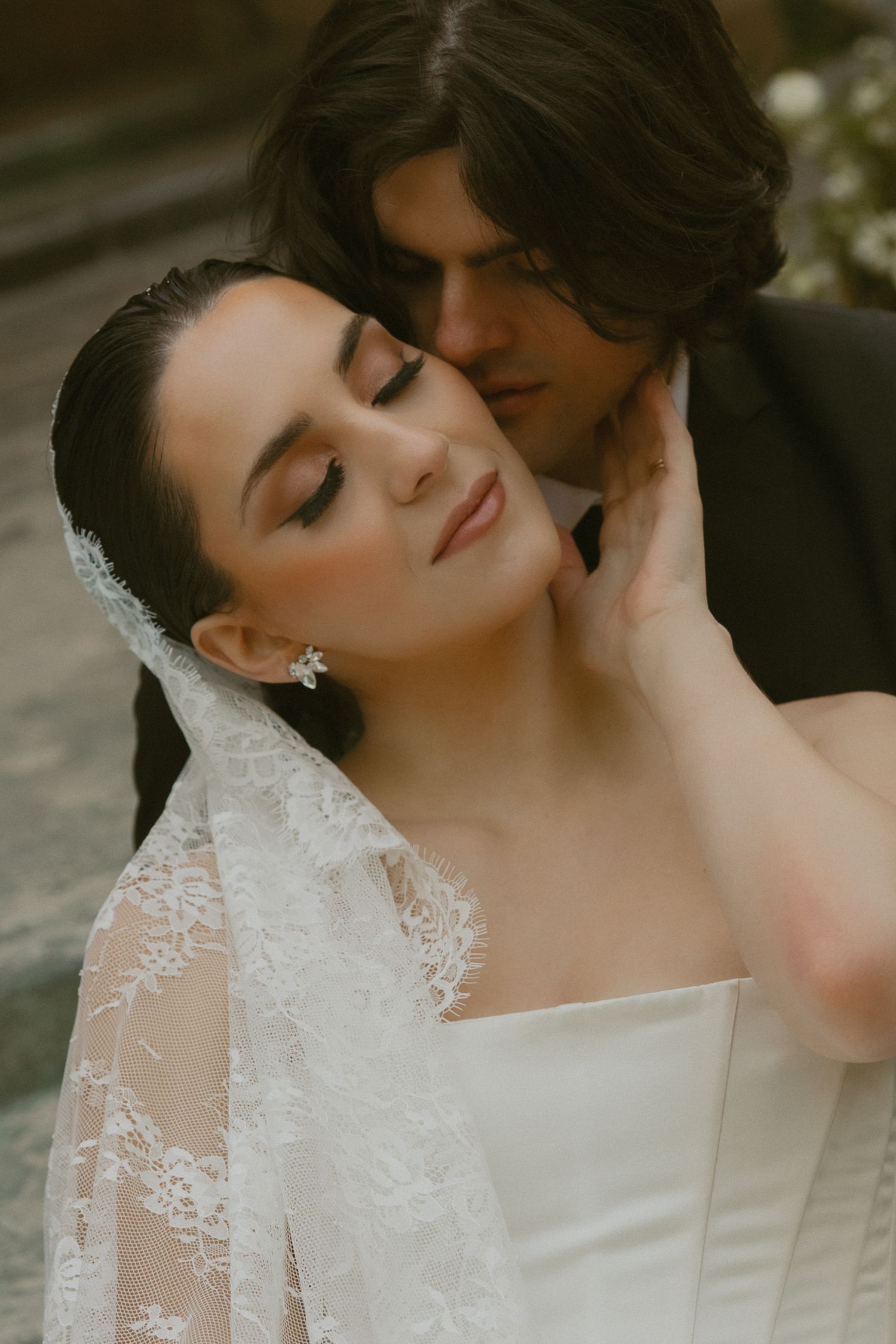A bride in a white lace wedding dress poses with closed eyes and elegant makeup in a romantic bridal portrait series.