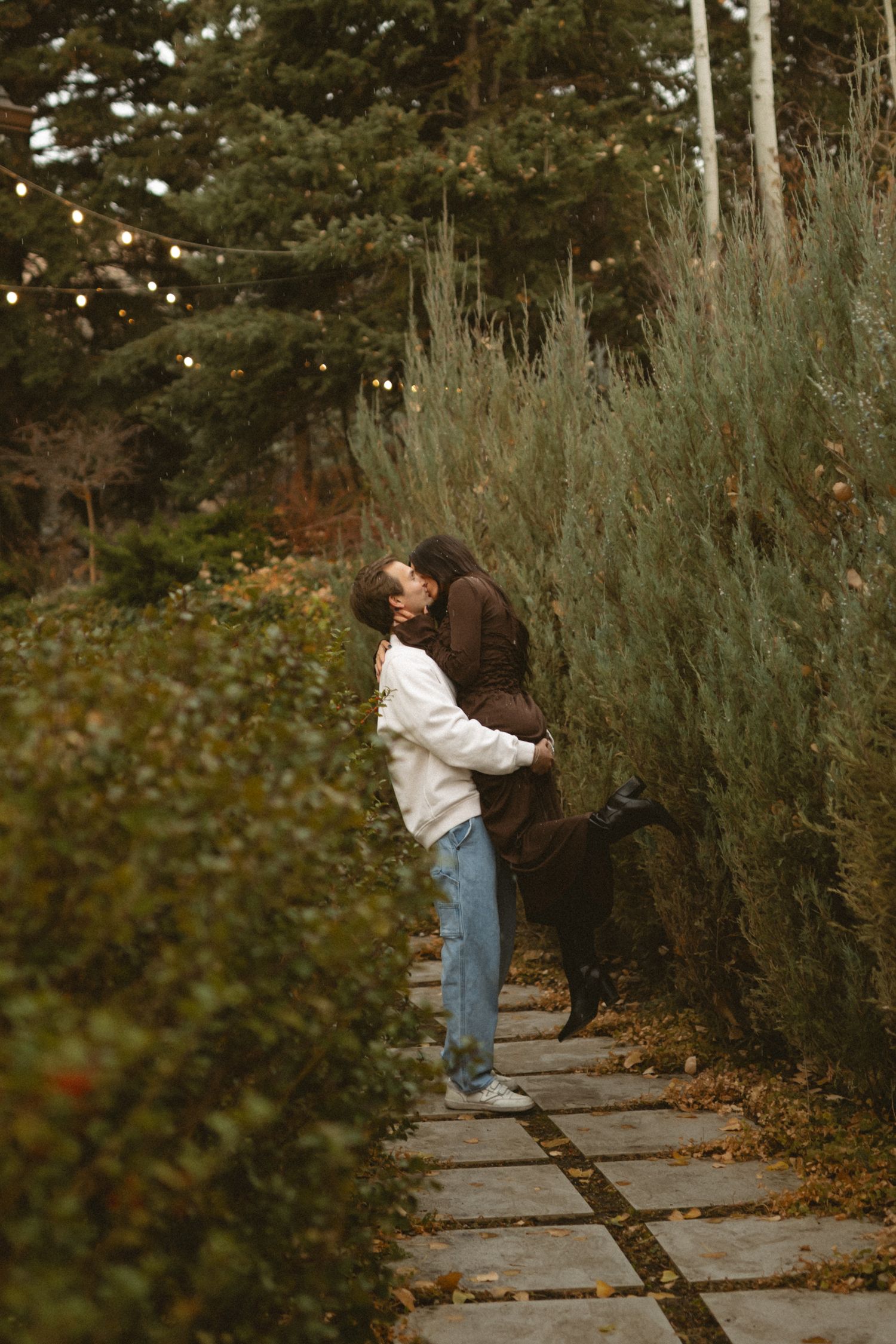 Couple sharing playful moments along a garden pathway surrounded by greenery.