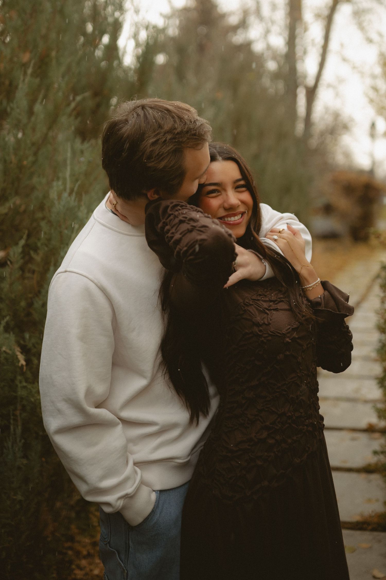 Couple laughing and embracing on autumn path with natural foliage backdrop.