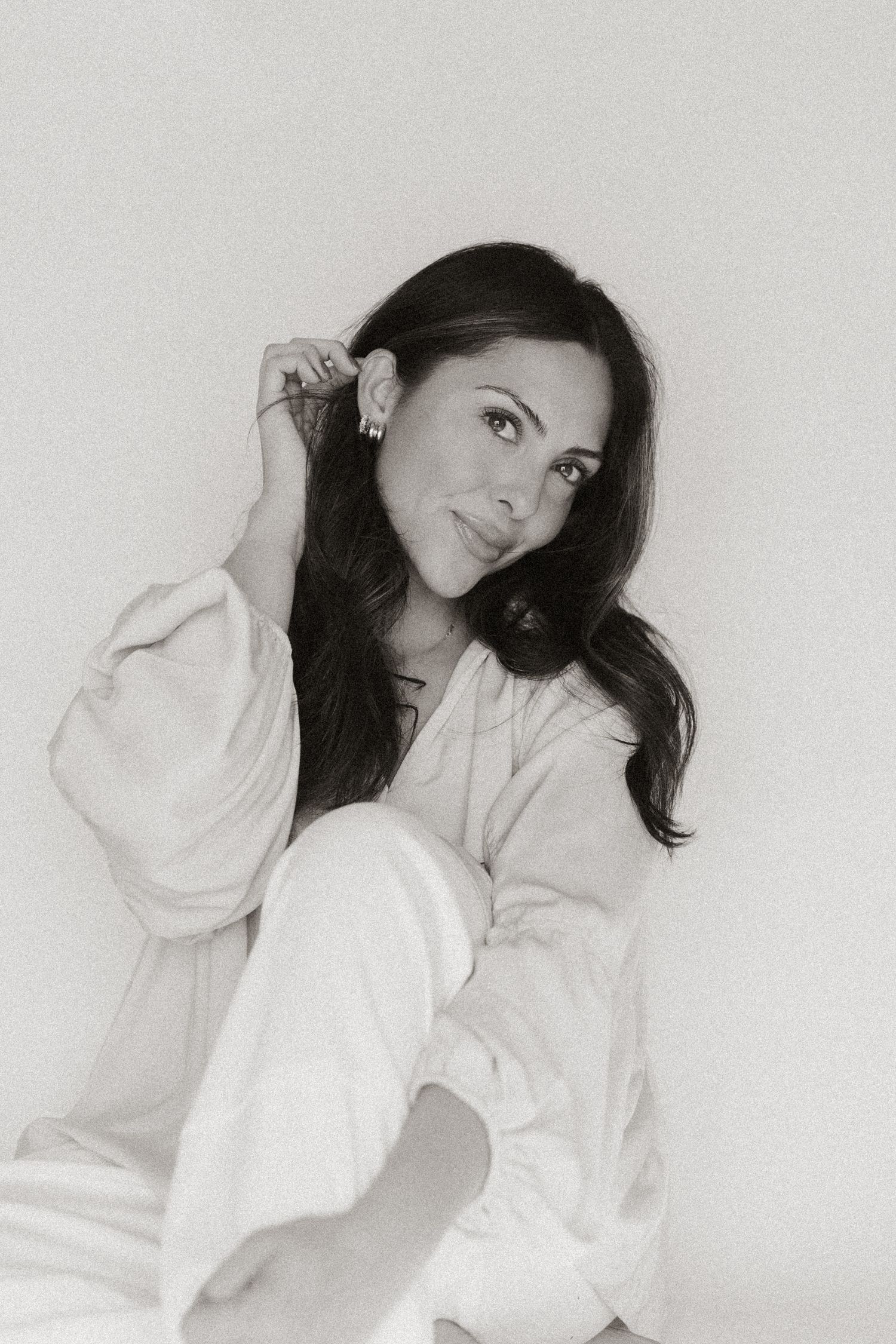 Black and white portrait of woman in white oversized sweater with flowing dark hair.
