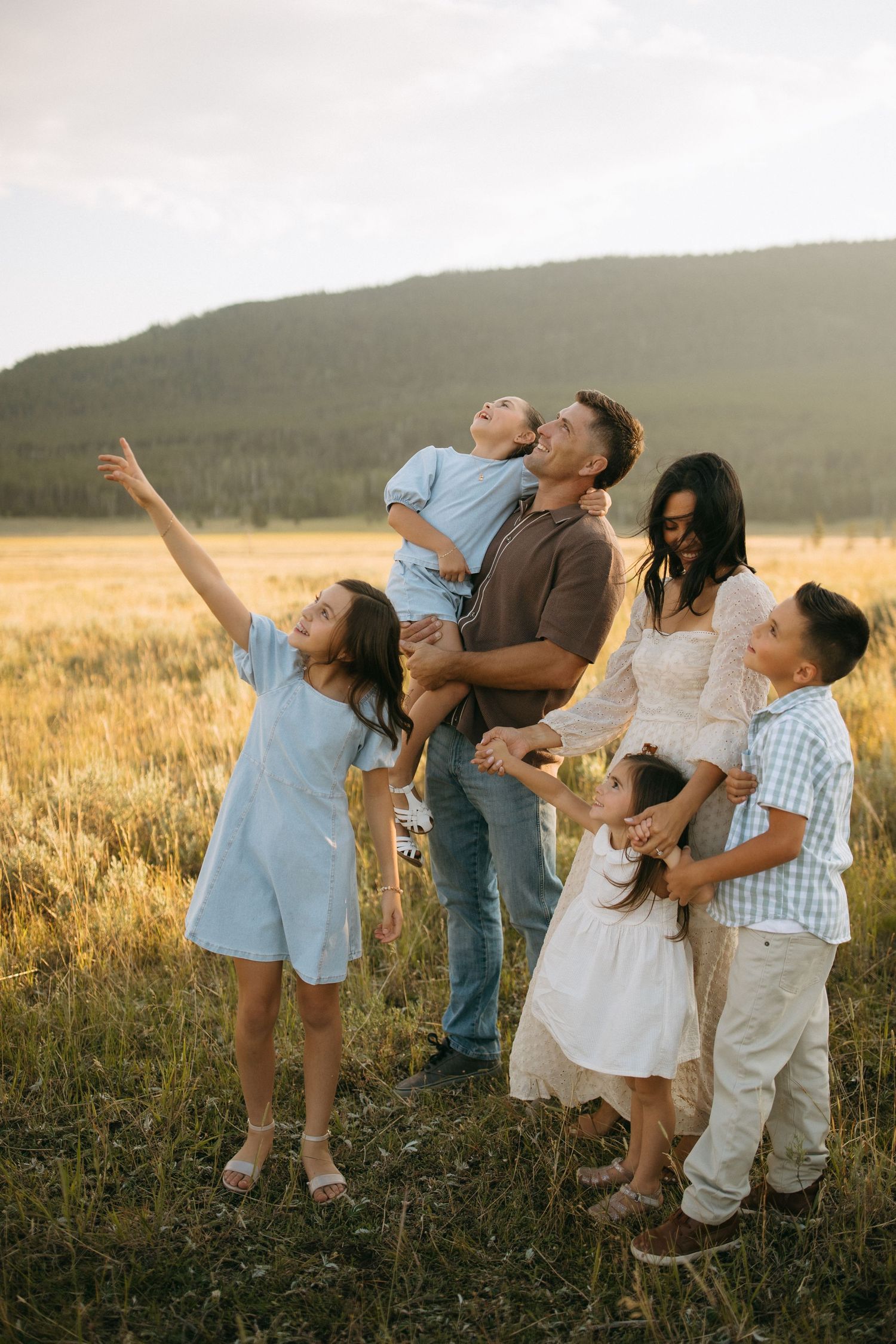 A group poses playfully in a field at sunset with mountains in the background.