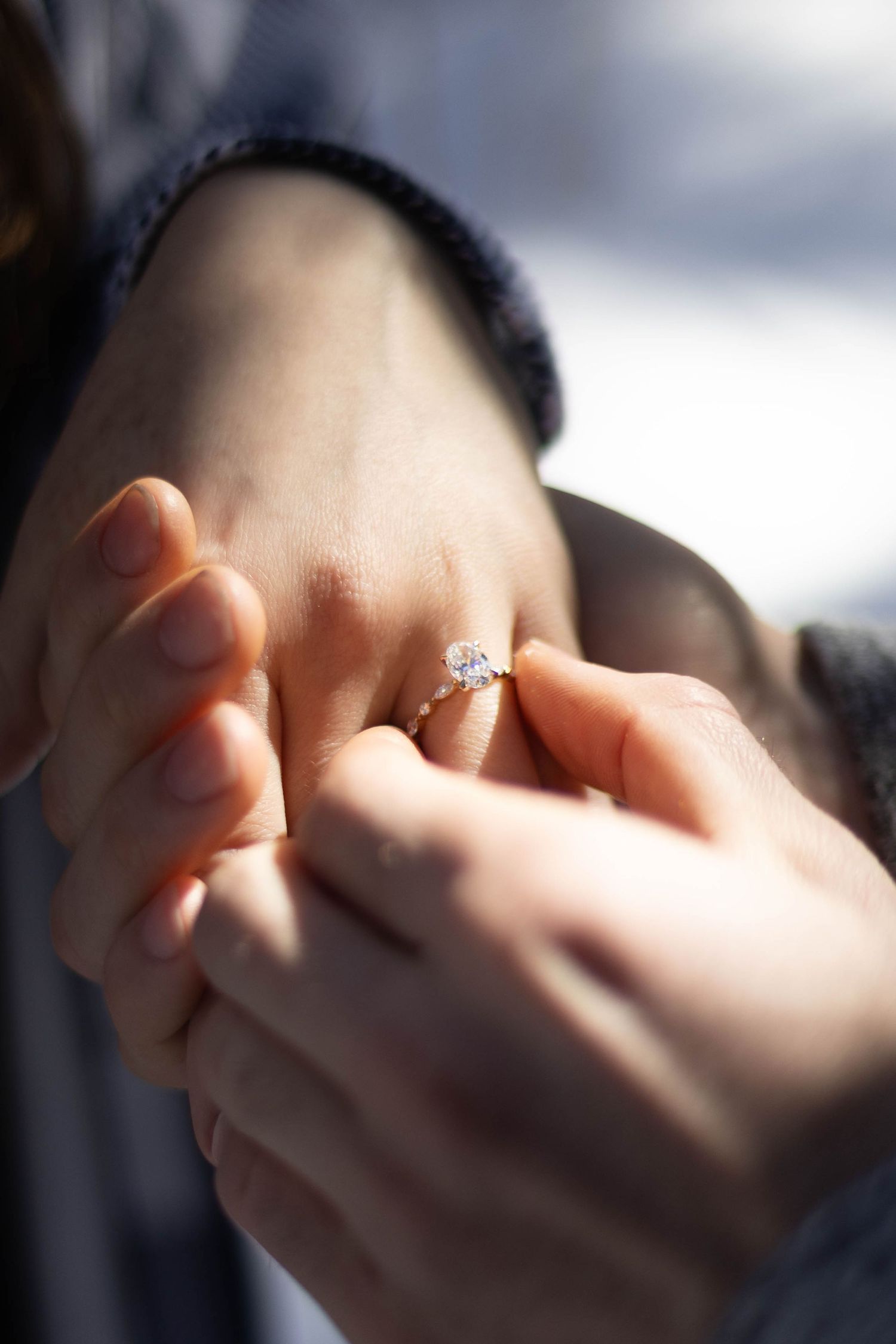 Close-up shot of hands holding a delicate engagement ring in soft focus.