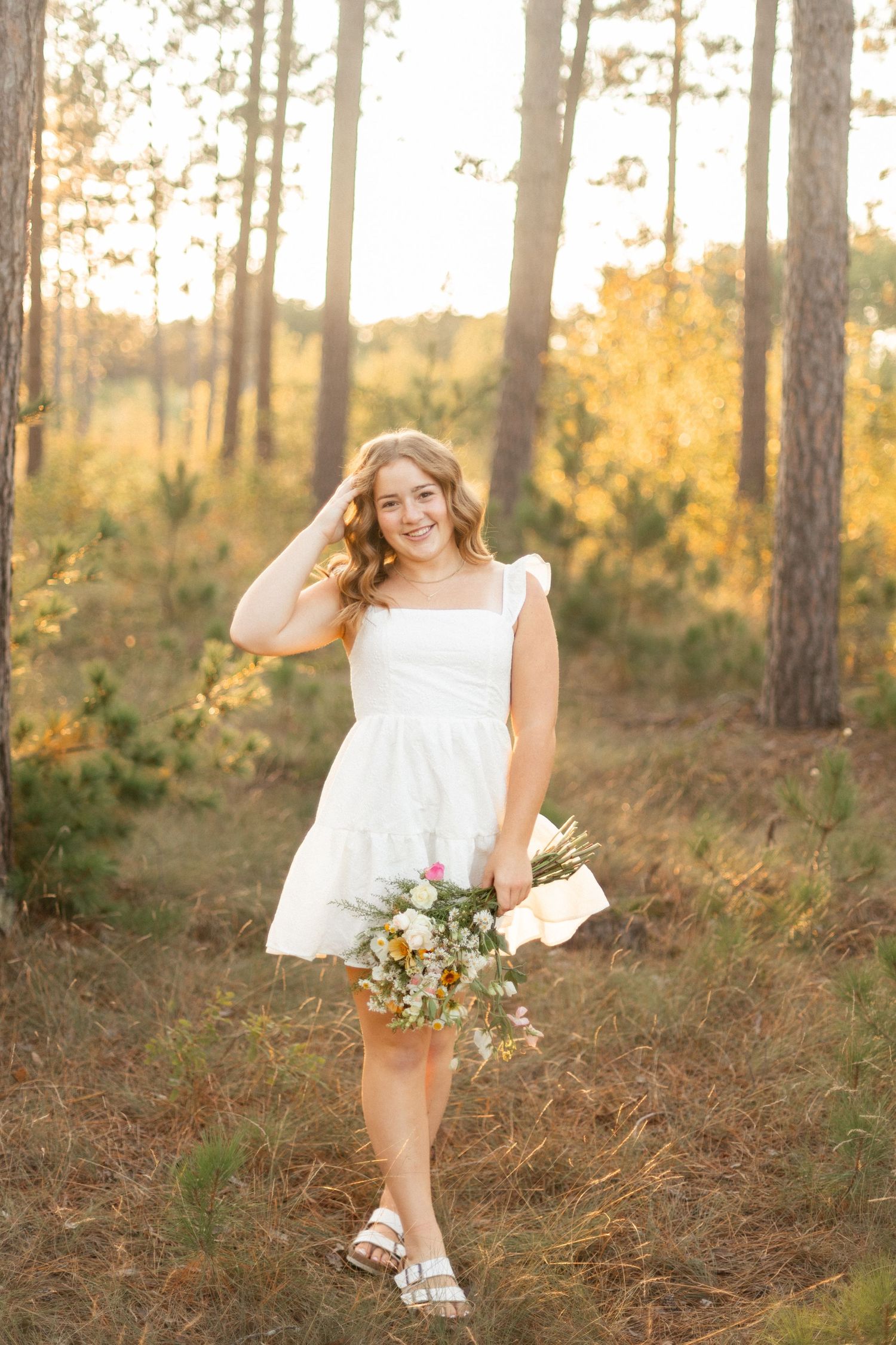 A white dress flows in the golden sunlight among tall pine trees.