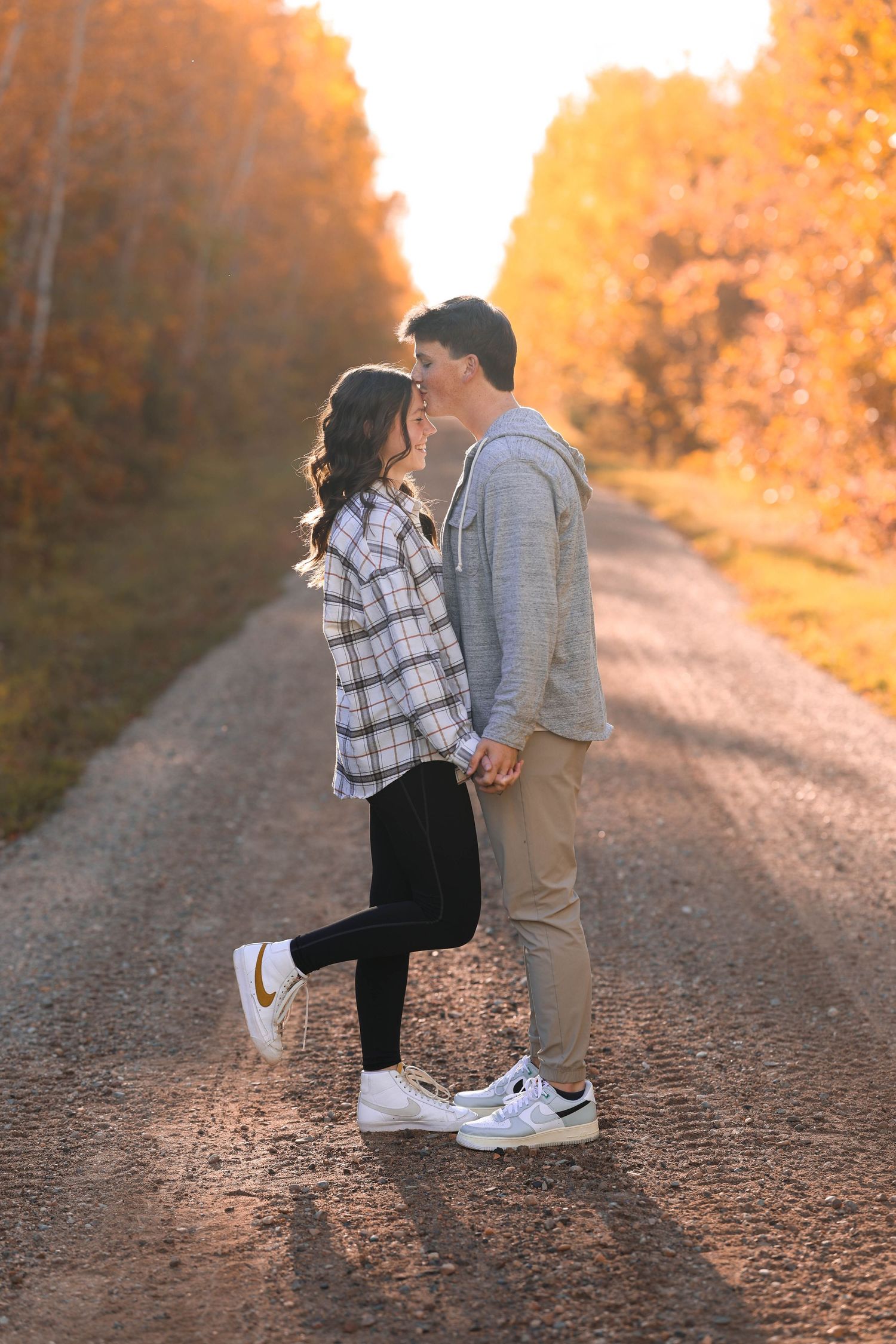 A couple in casual attire sharing a romantic moment on a sunset-lit gravel path.