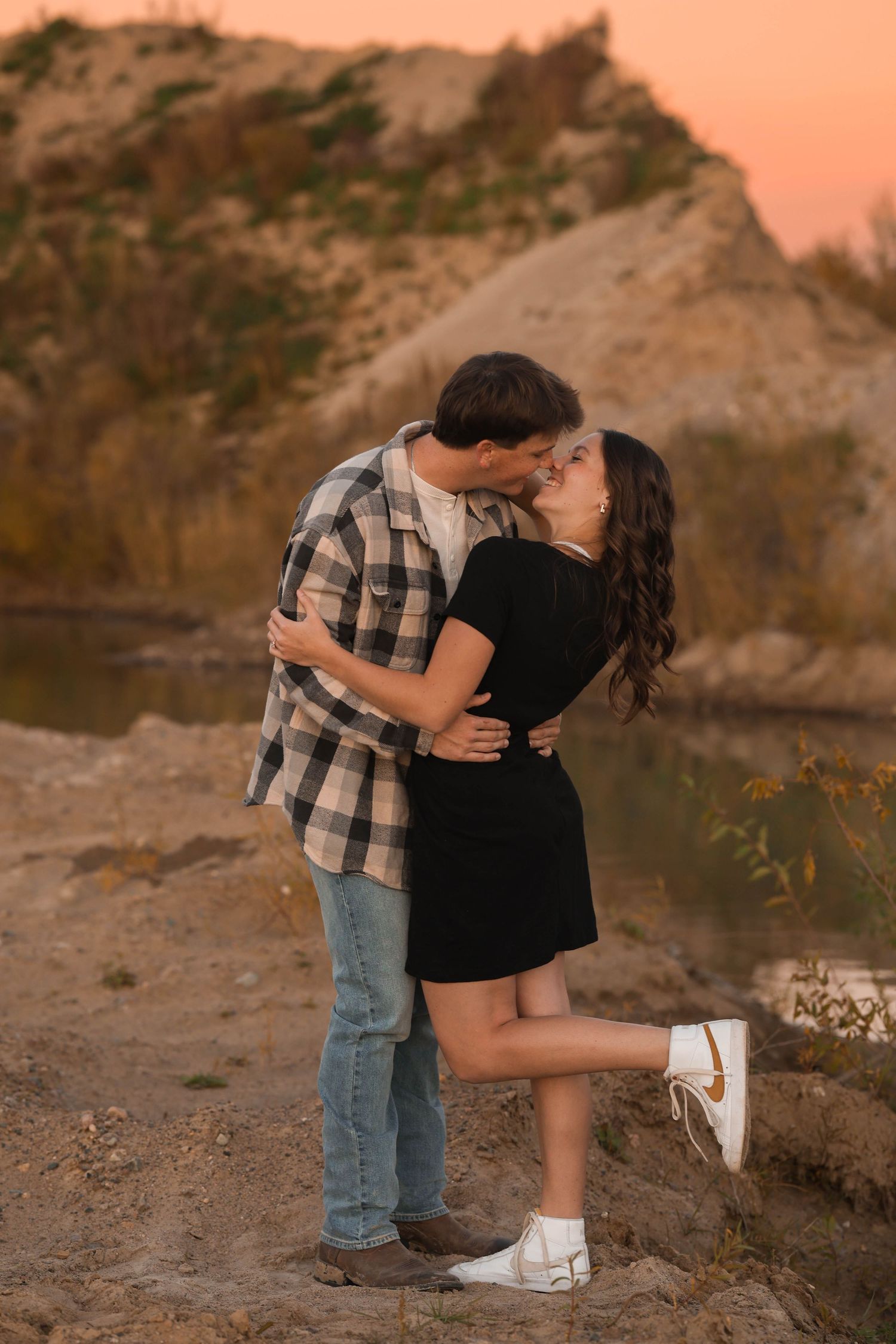 A couple sharing a romantic moment near rocky terrain during golden hour.