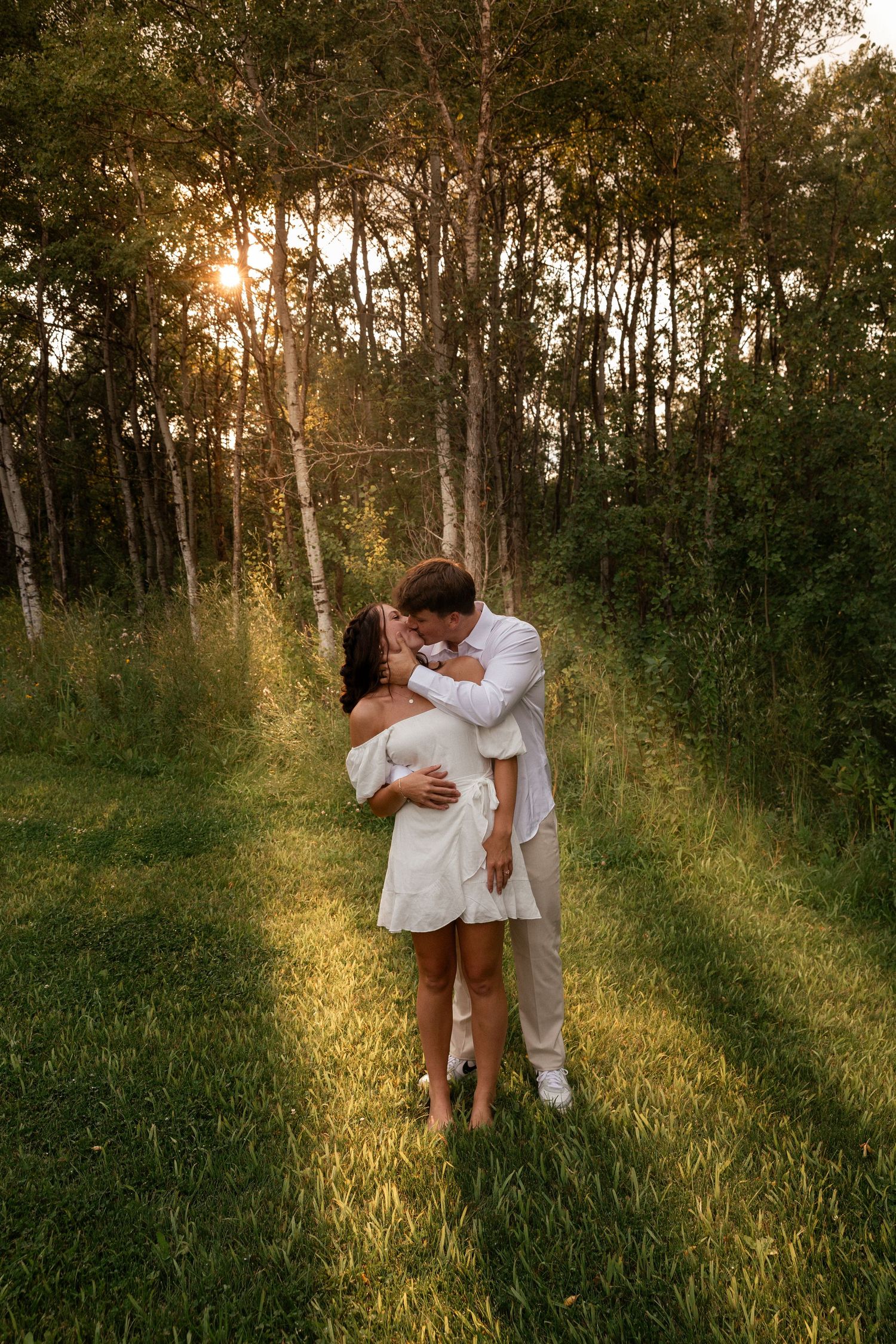 A couple embraces lovingly in a sunlit forest setting during golden hour.