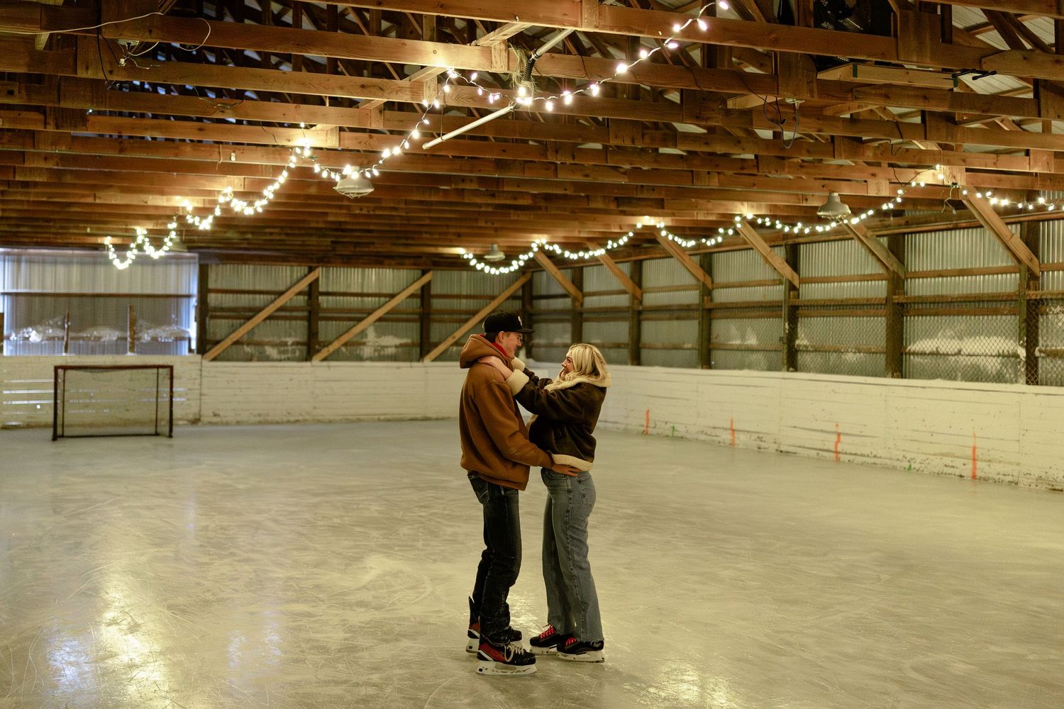 String lights illuminate an indoor ice skating rink where people practice skating techniques with an instructor.