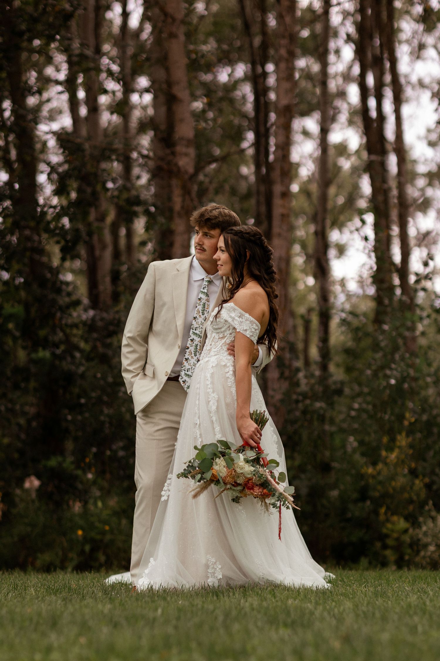 Elegant wedding couple poses in a rustic forest setting during golden hour.