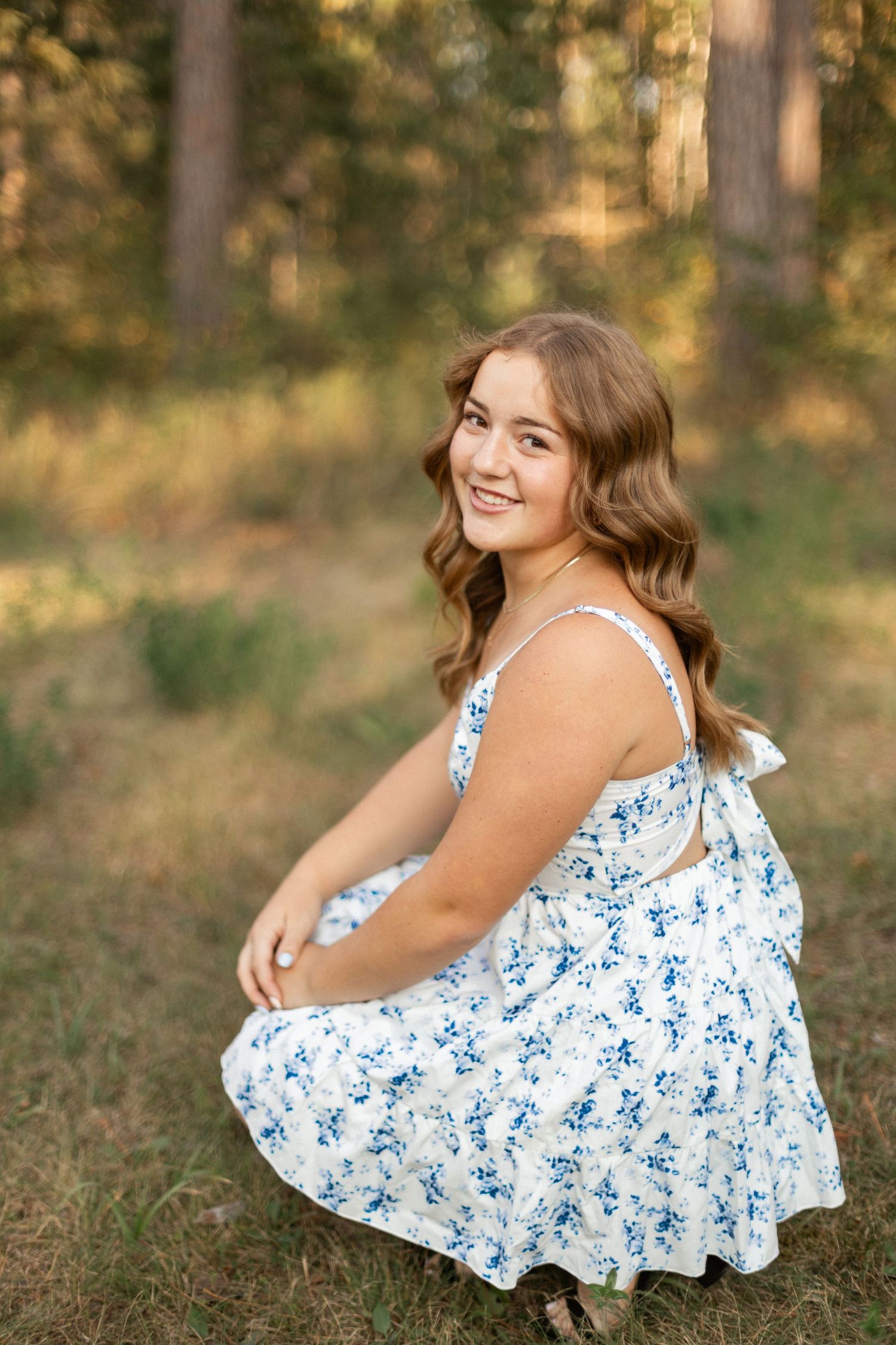 A person in a blue floral dress poses gracefully in a natural outdoor setting.