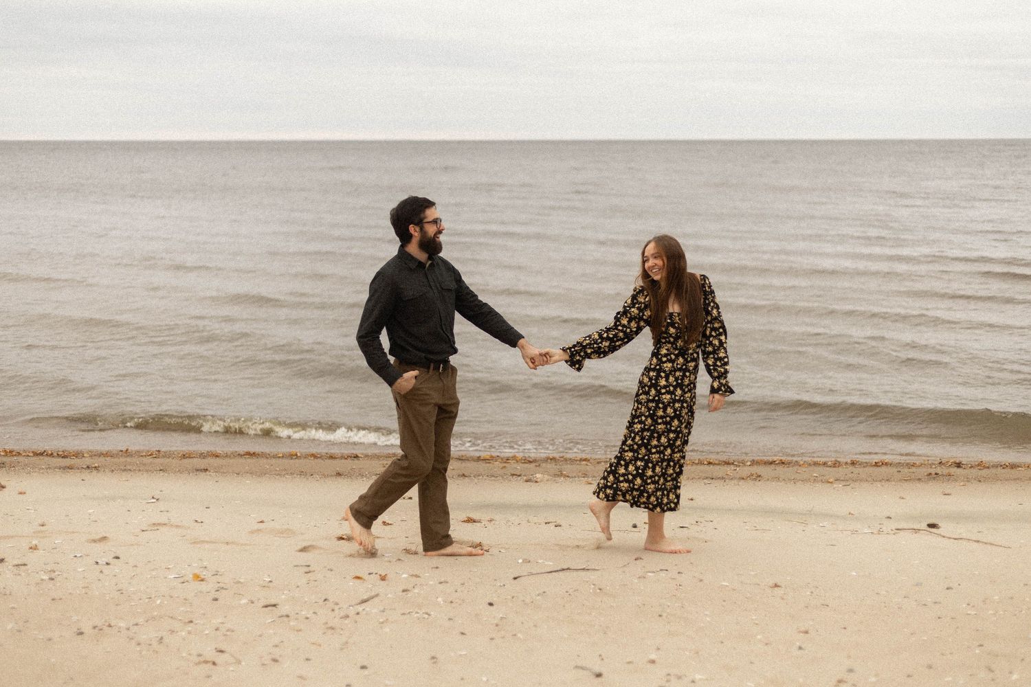 A playful couple runs and dances on a cloudy beach.