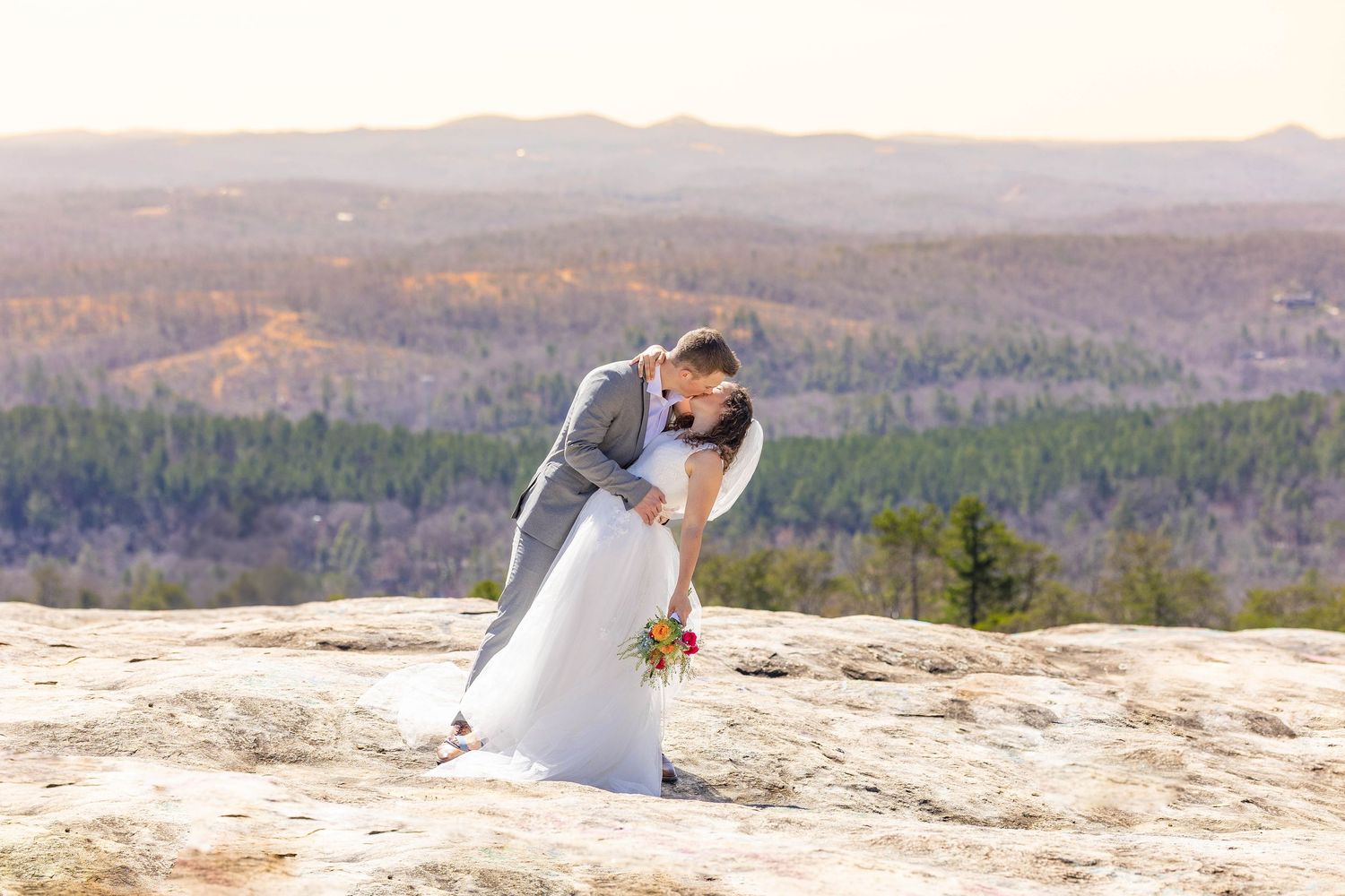 A wedding couple embraces on a mountaintop with sweeping valley views.
