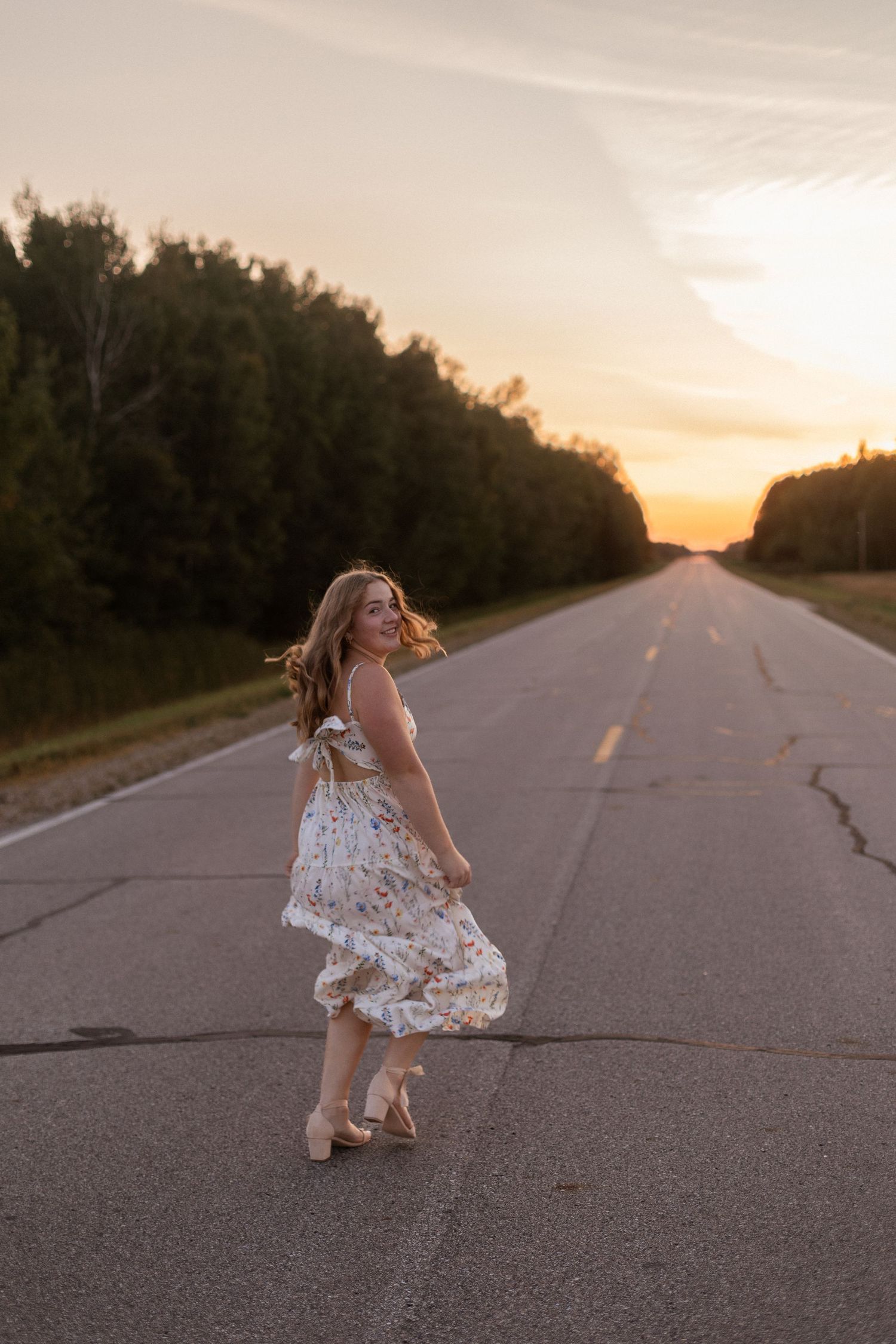 A person in a white dress dances on an empty road at sunset.