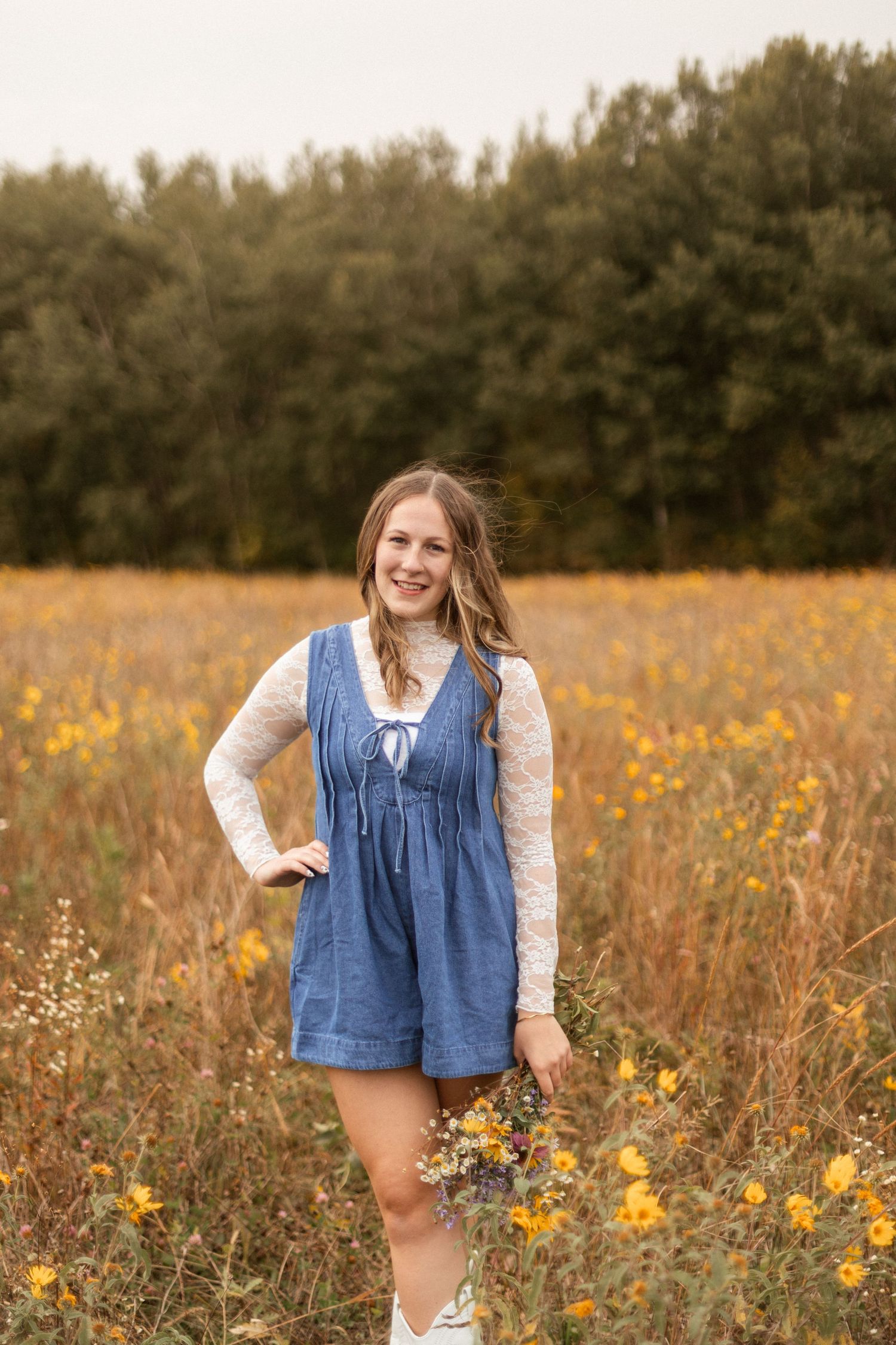 A person poses among yellow wildflowers wearing denim and white lace.