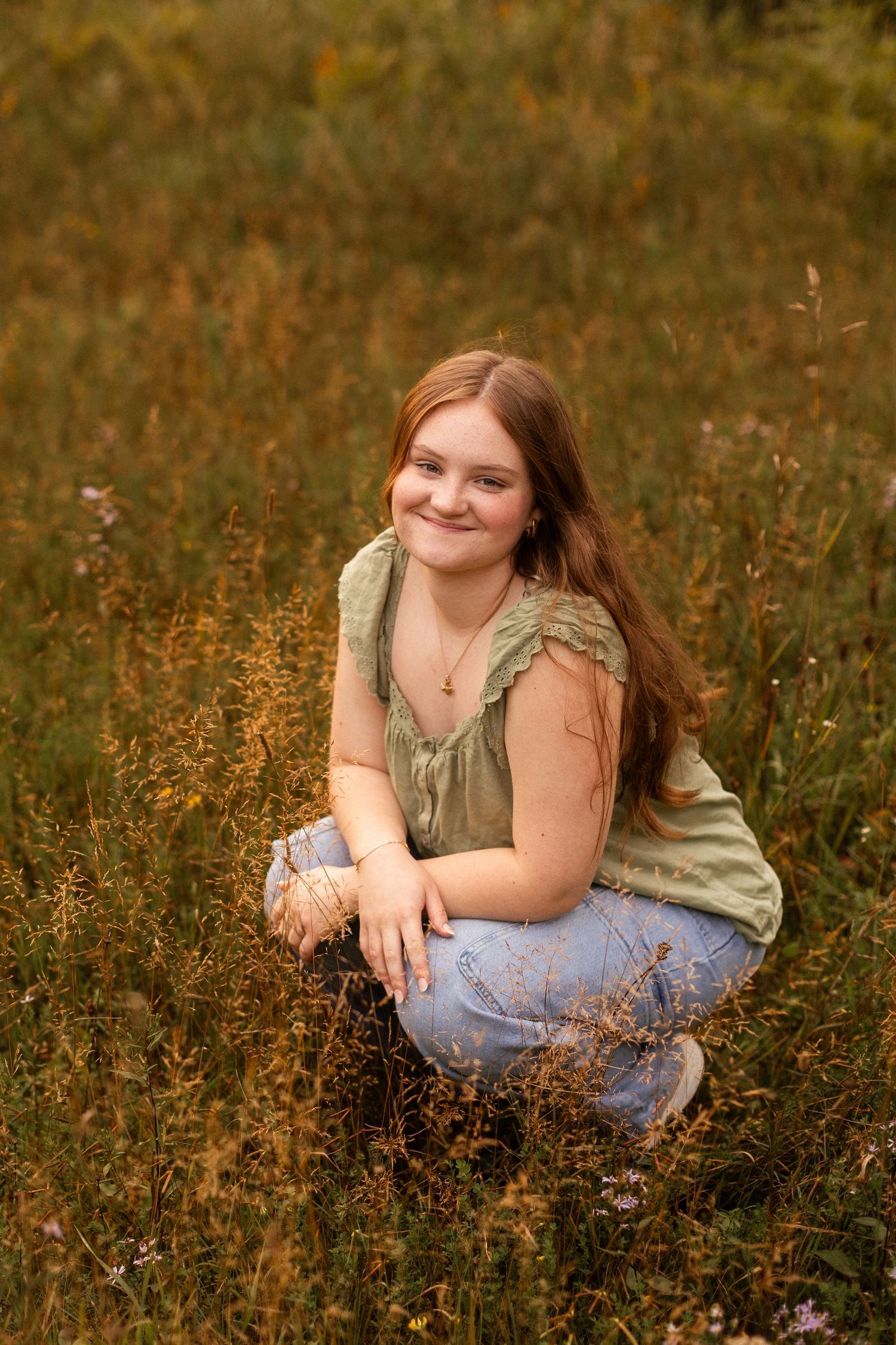A person in a sage green top poses casually in a wildflower meadow at sunset.