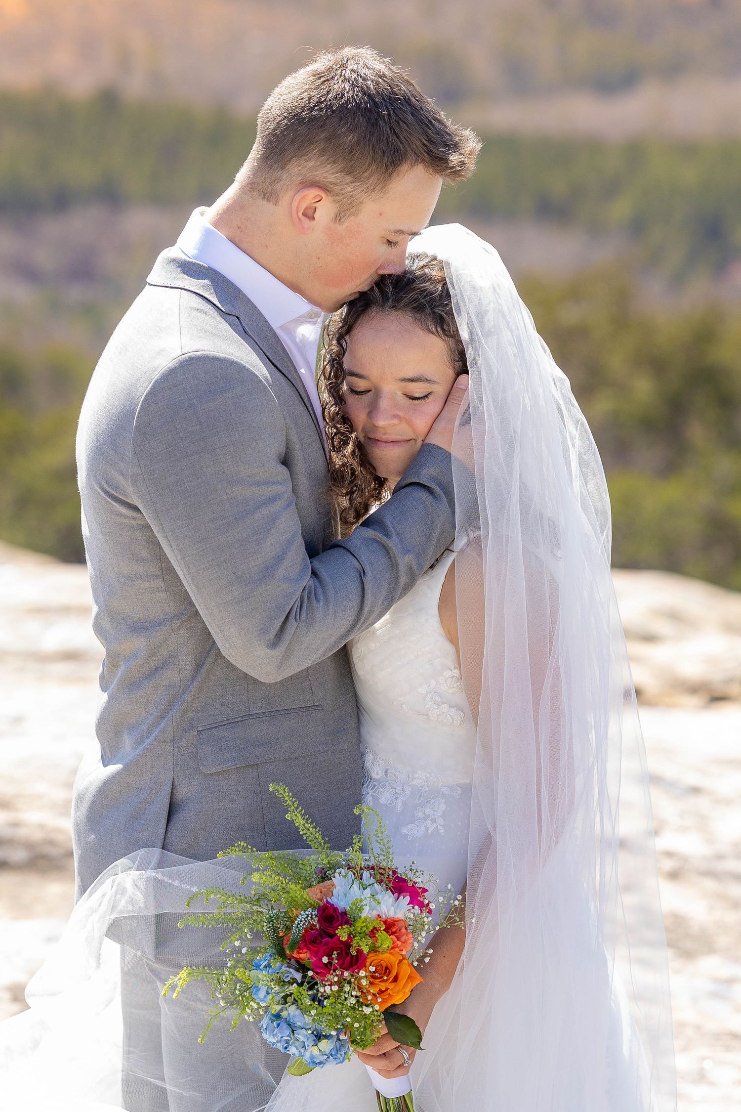 A couple shares an intimate moment with colorful bouquet against mountain backdrop.