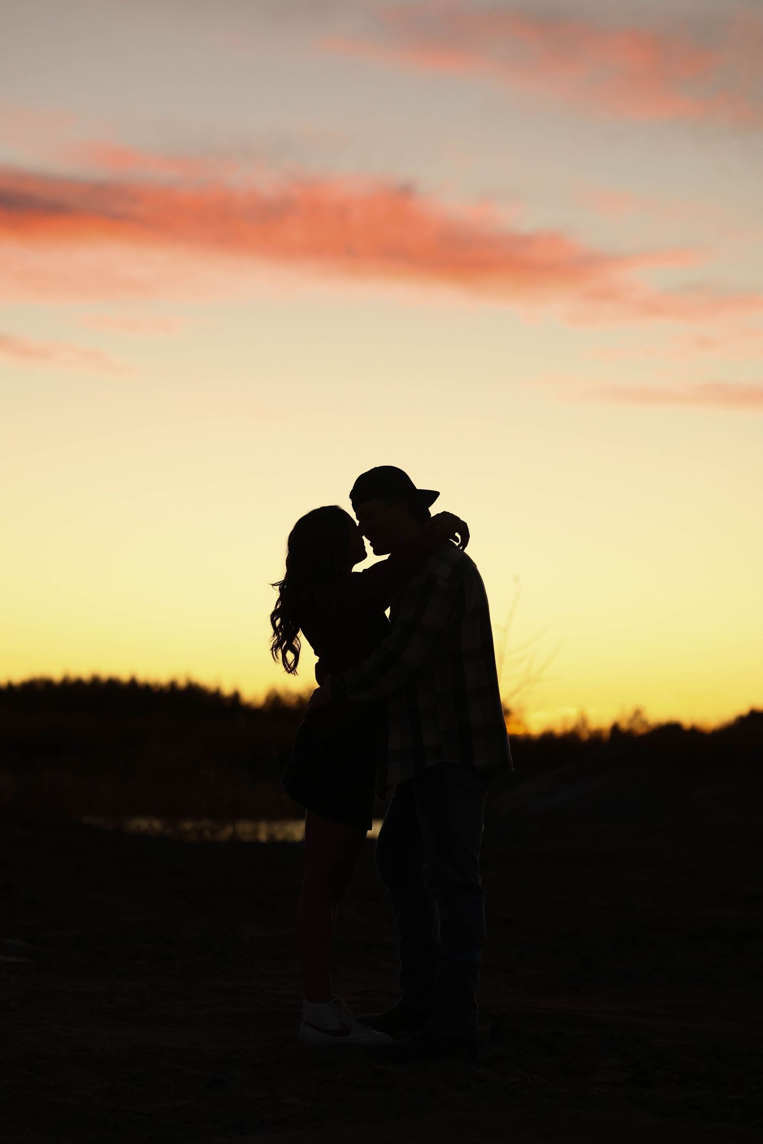 Silhouettes of two people in an intimate moment against a dramatic sunset sky.
