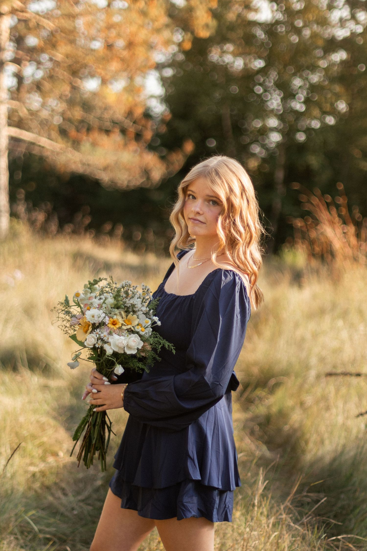 A person in navy blue holds a bouquet of wildflowers in golden evening light.