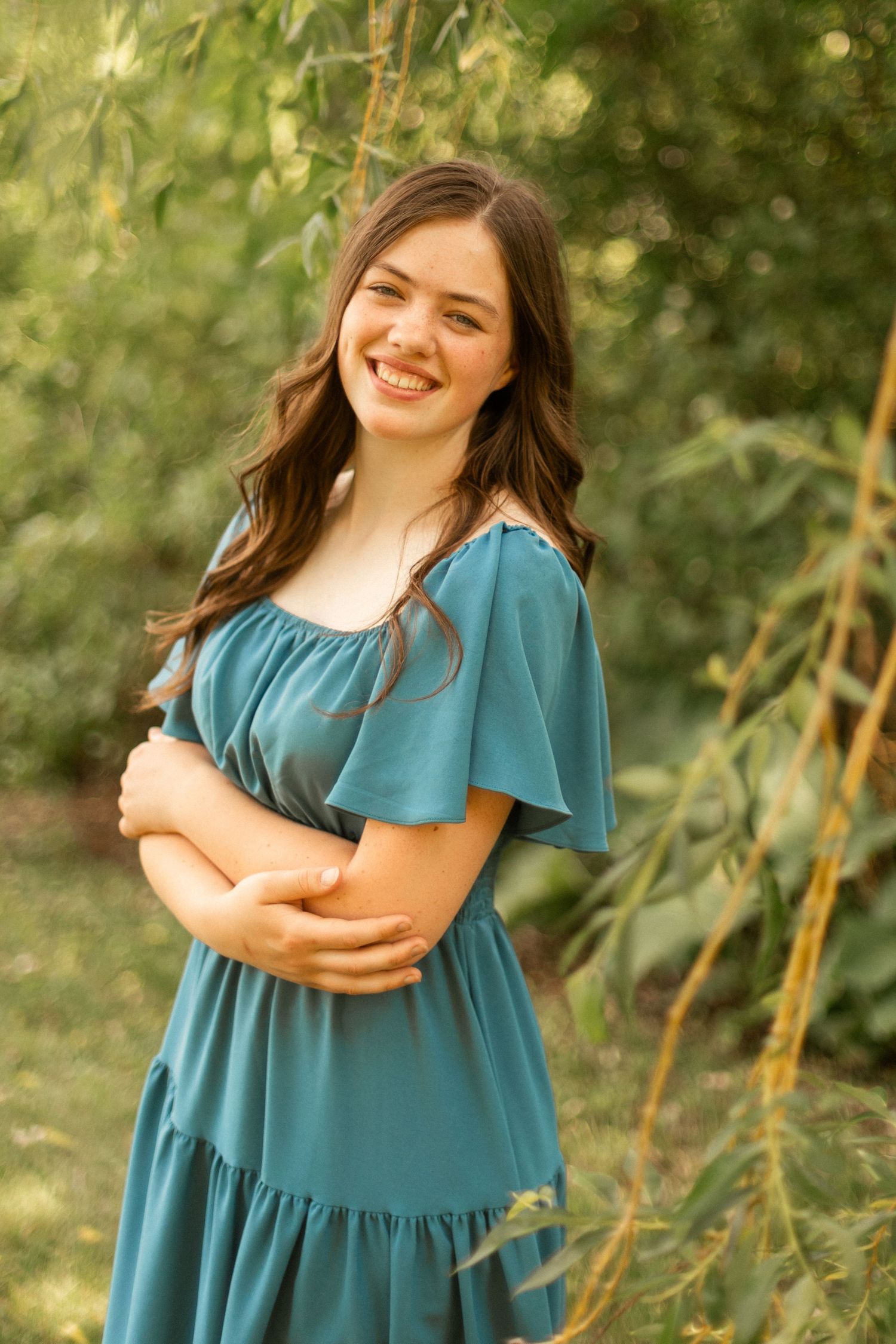 A person in a teal dress poses outdoors against a natural green background.