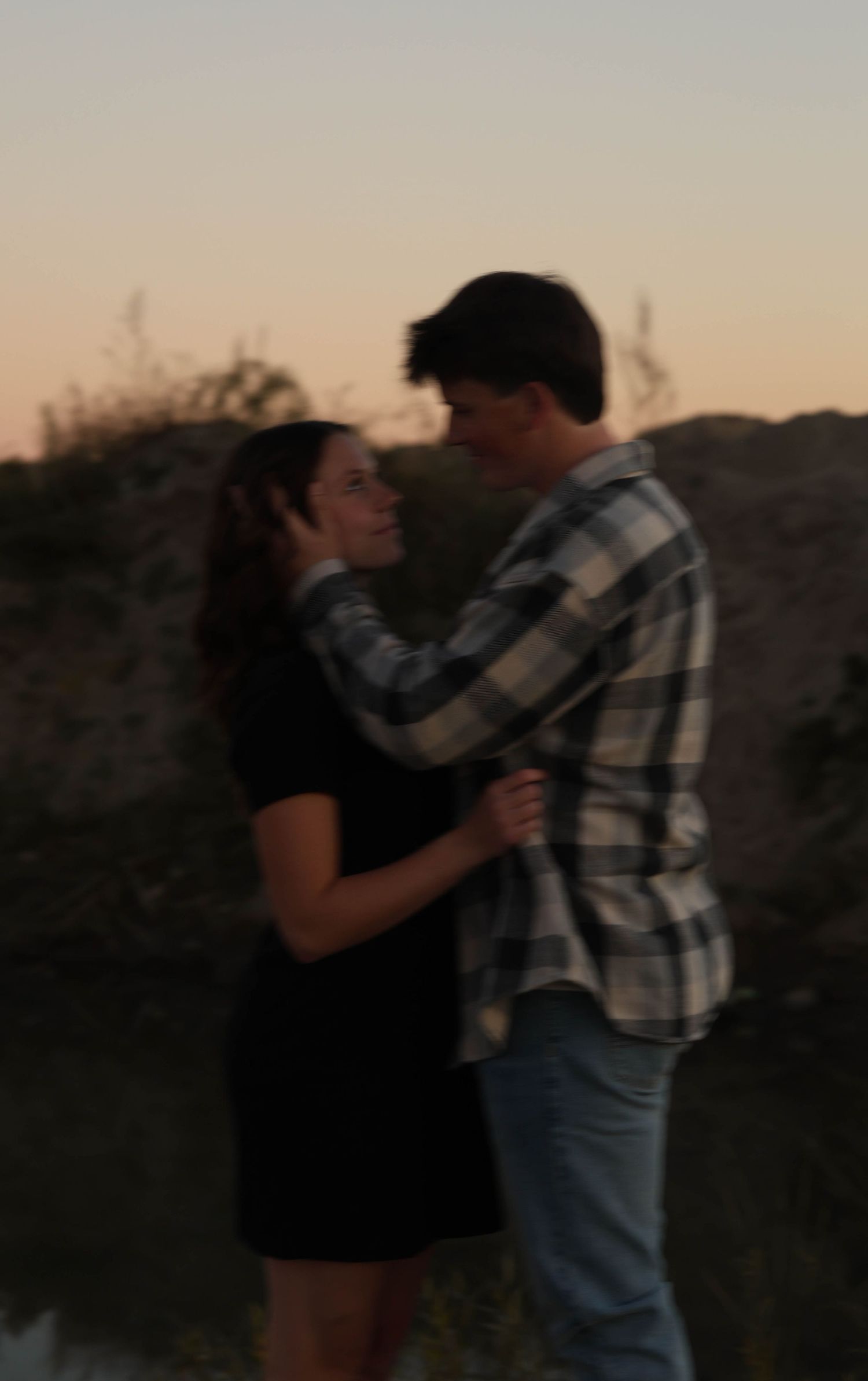 A couple embracing at dusk with warm sunset lighting in the background.