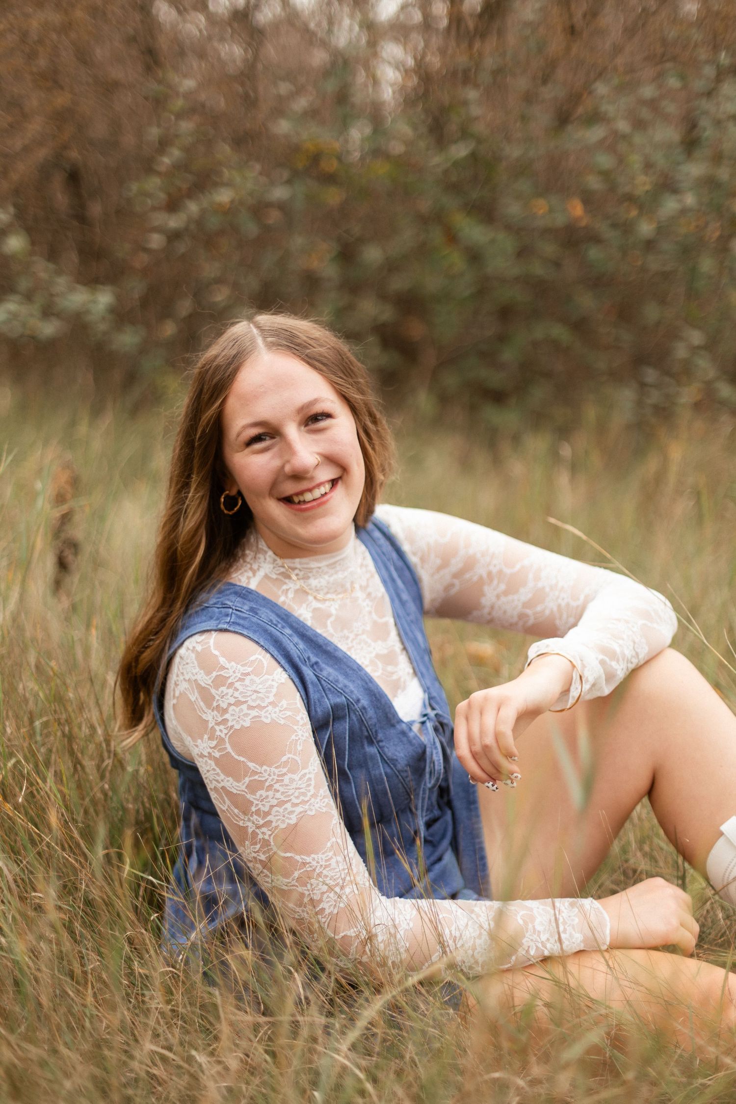 A person in denim and lace lounges in tall grass during an outdoor photoshoot.