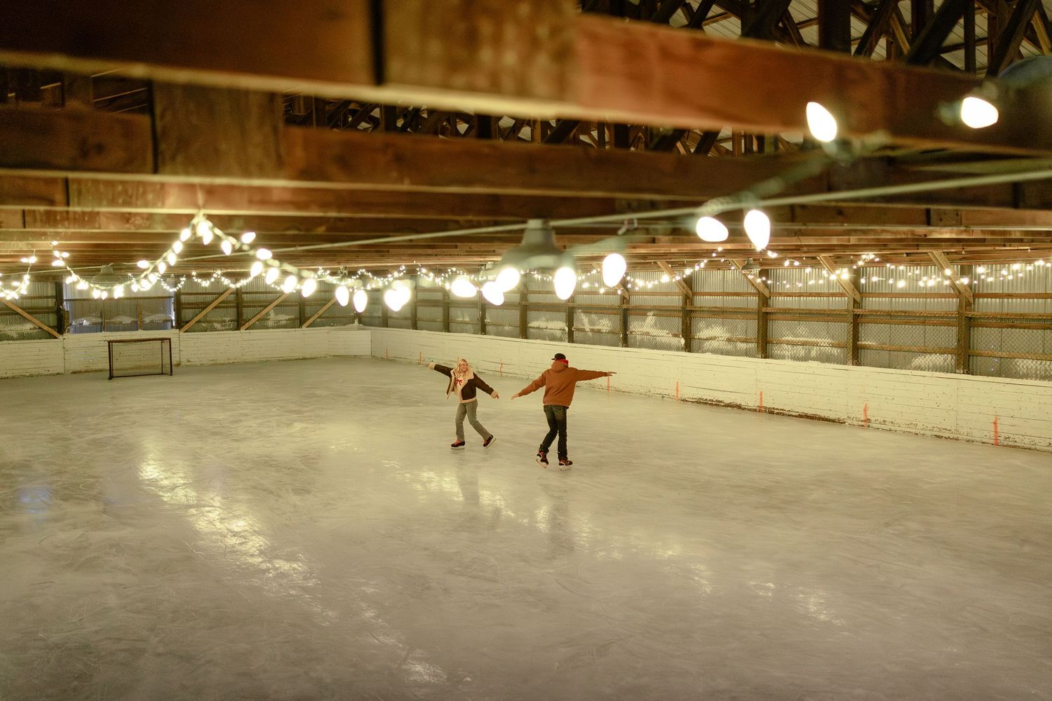 Indoor ice skating rink with warm lighting illuminating the smooth skating surface and surrounding wooden walls.