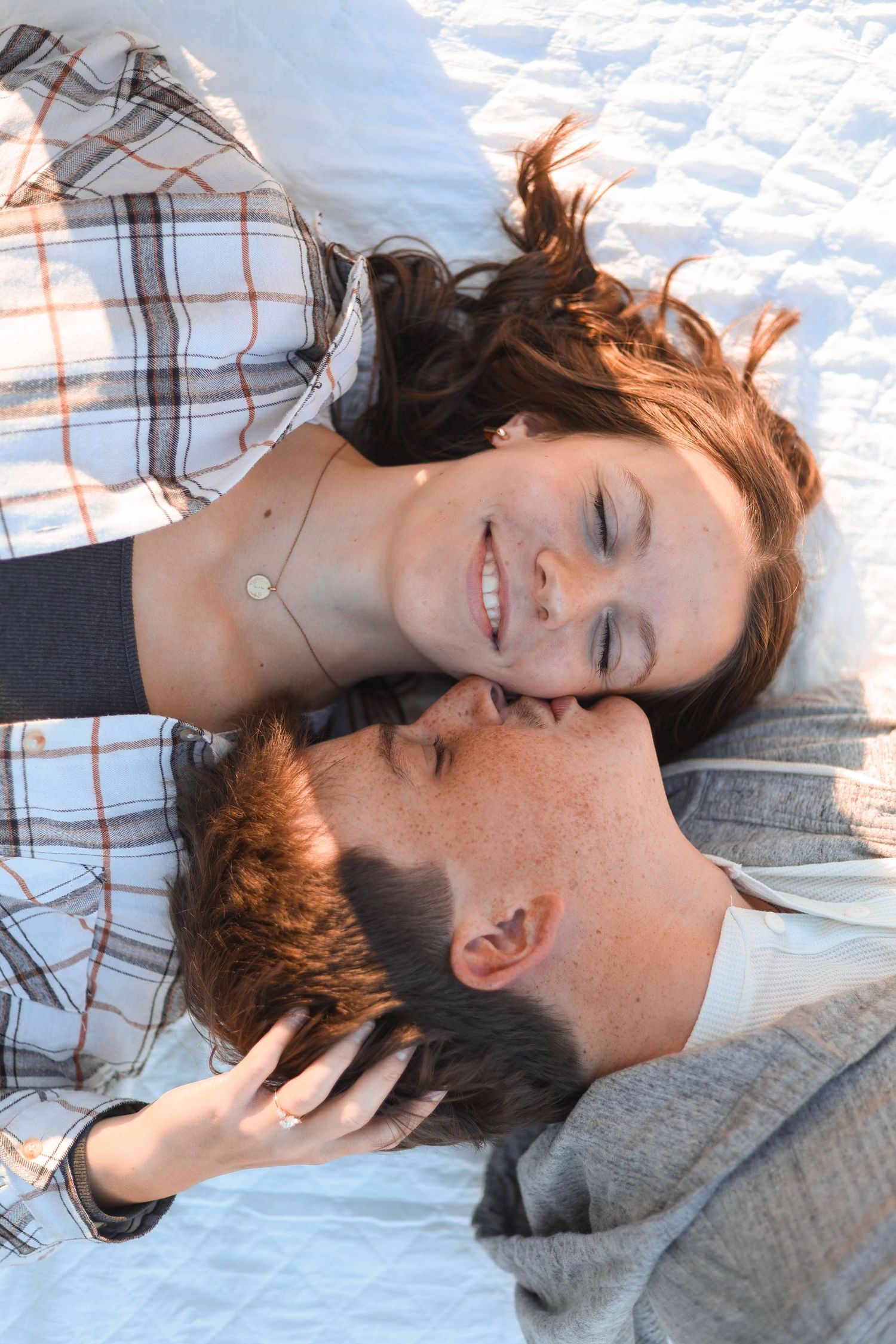 A couple lying close together on a white blanket outdoors.