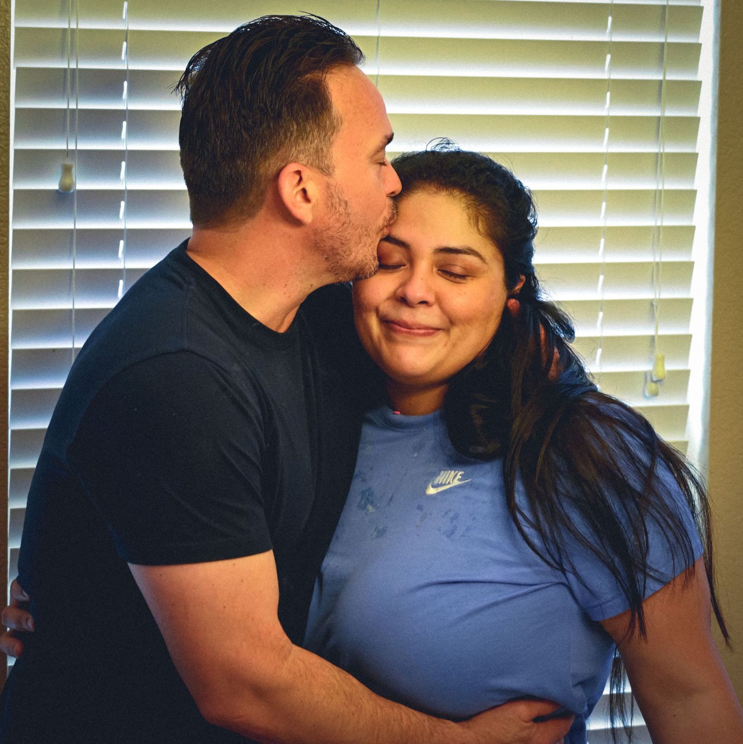 Intimate couple sharing affectionate moments against window blinds background.