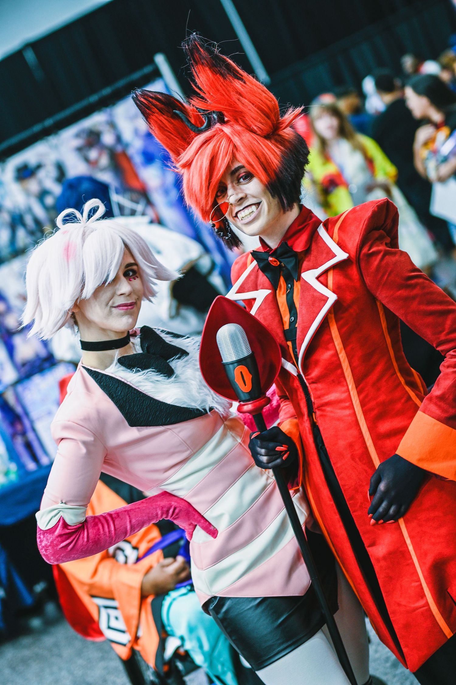 Cosplayers in bright red and pink outfits posing together at convention.