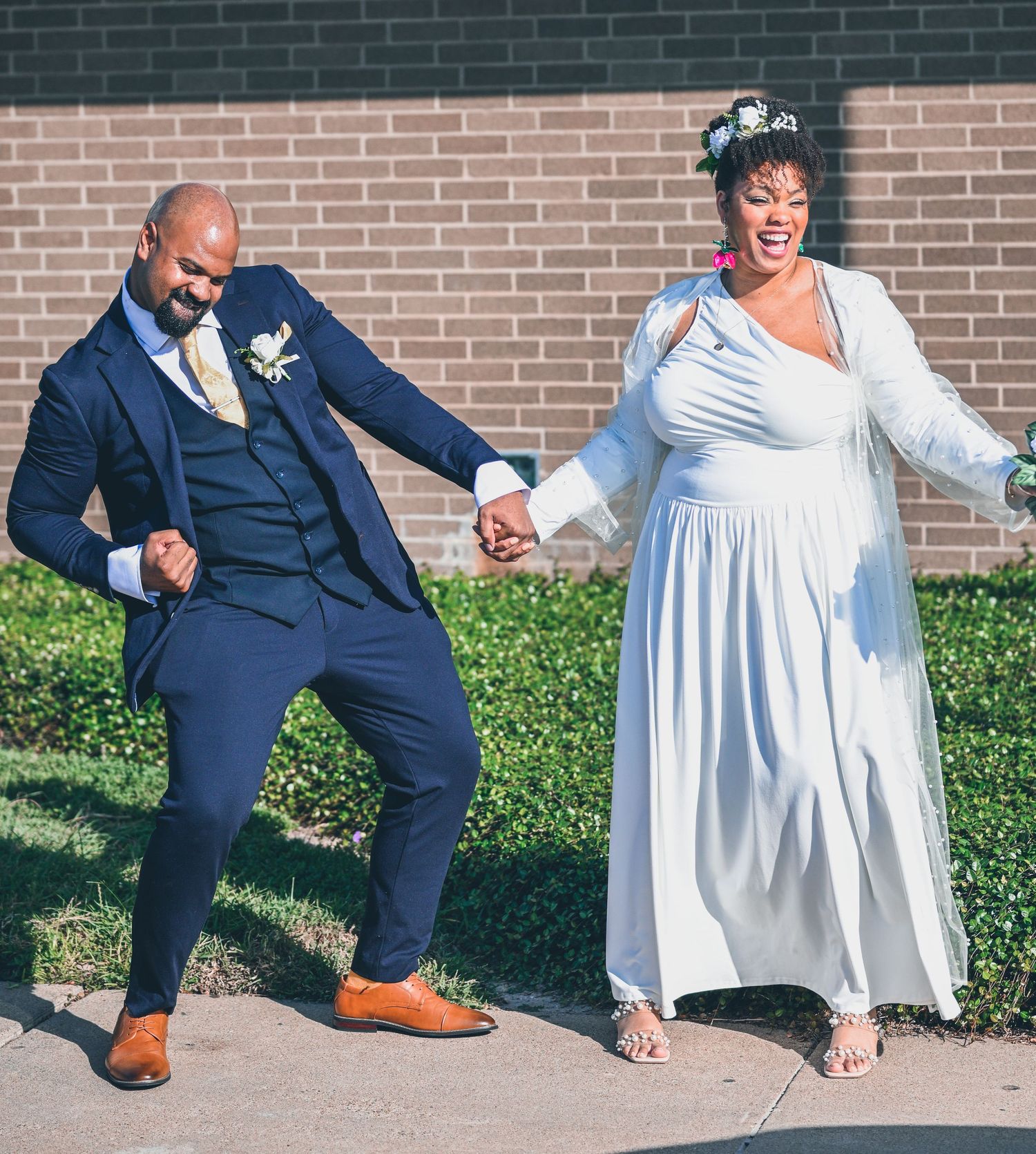 Wedding party showing fun dance poses against a brick wall background.