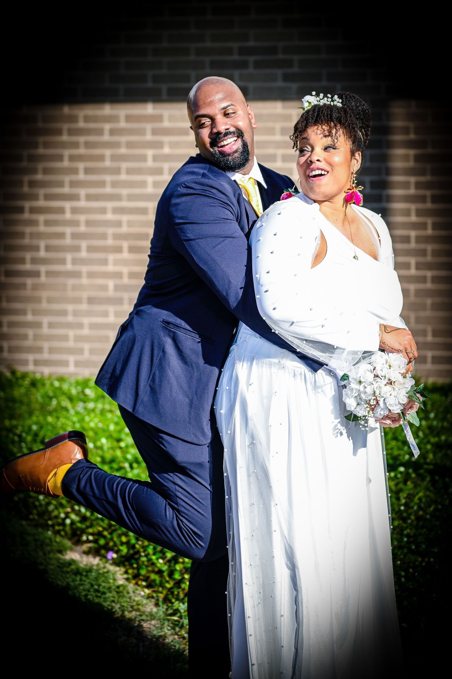 Romantic wedding portraits against a brick wall with dramatic lighting and white dress.