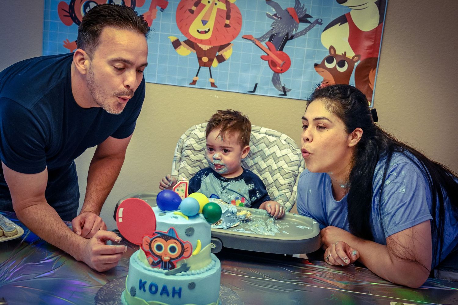 Family celebrating with a blue monster themed birthday cake and decorations.