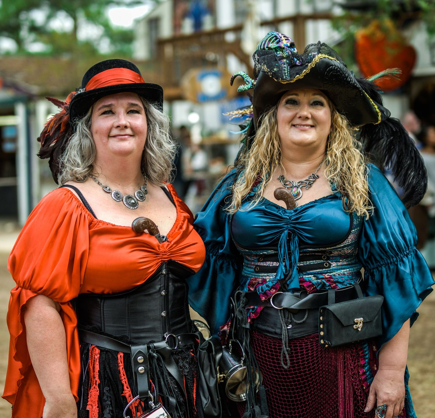 Group of women in steampunk costumes with corsets and hats pose outdoors.